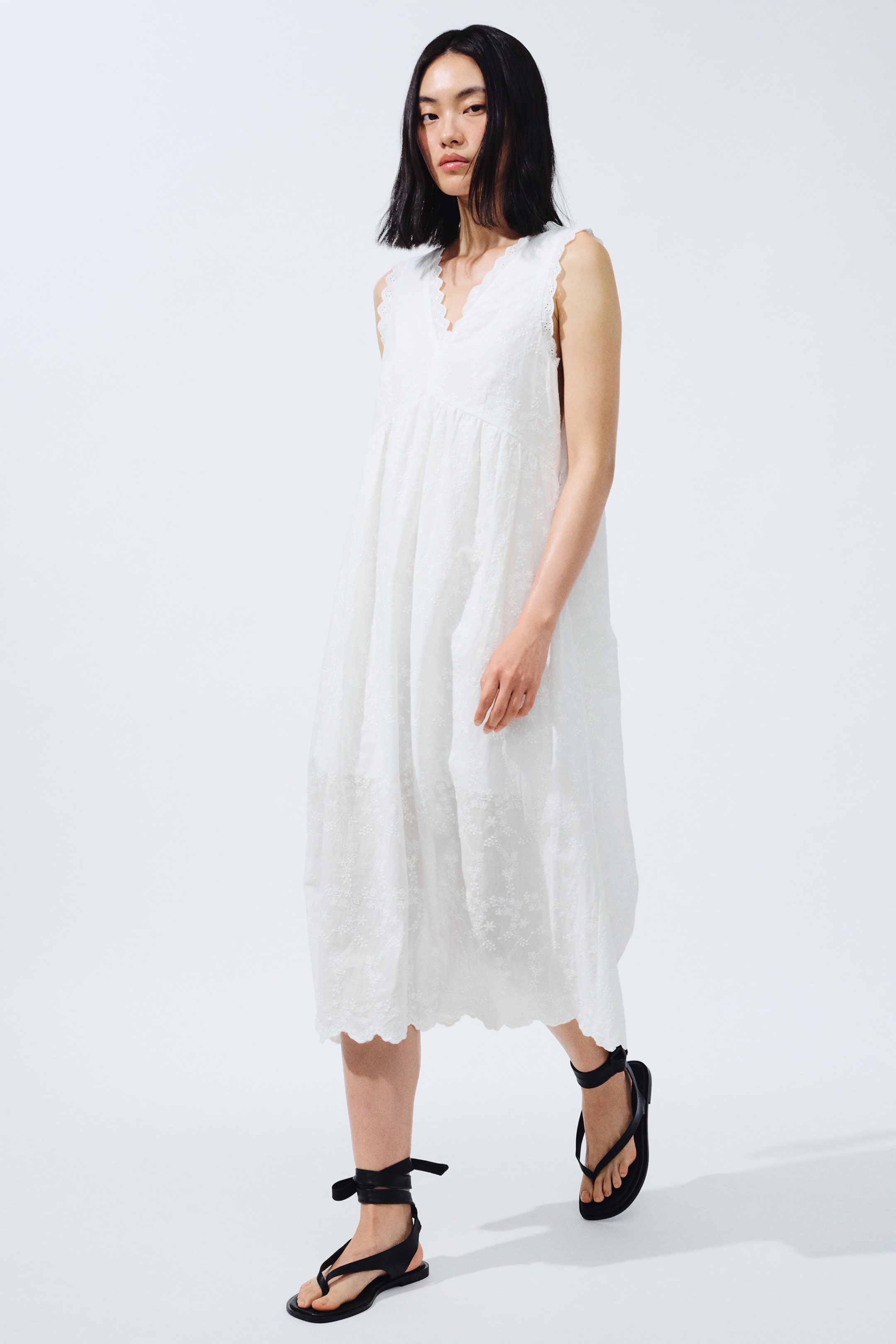 View larger image: A white sleeveless midi dress featuring a V-neckline and armholes with scalloped edges. The dress showcases an embroidered floral pattern throughout its relaxed, flowing silhouette, gathering below the bust and finishing with a scalloped hemline.