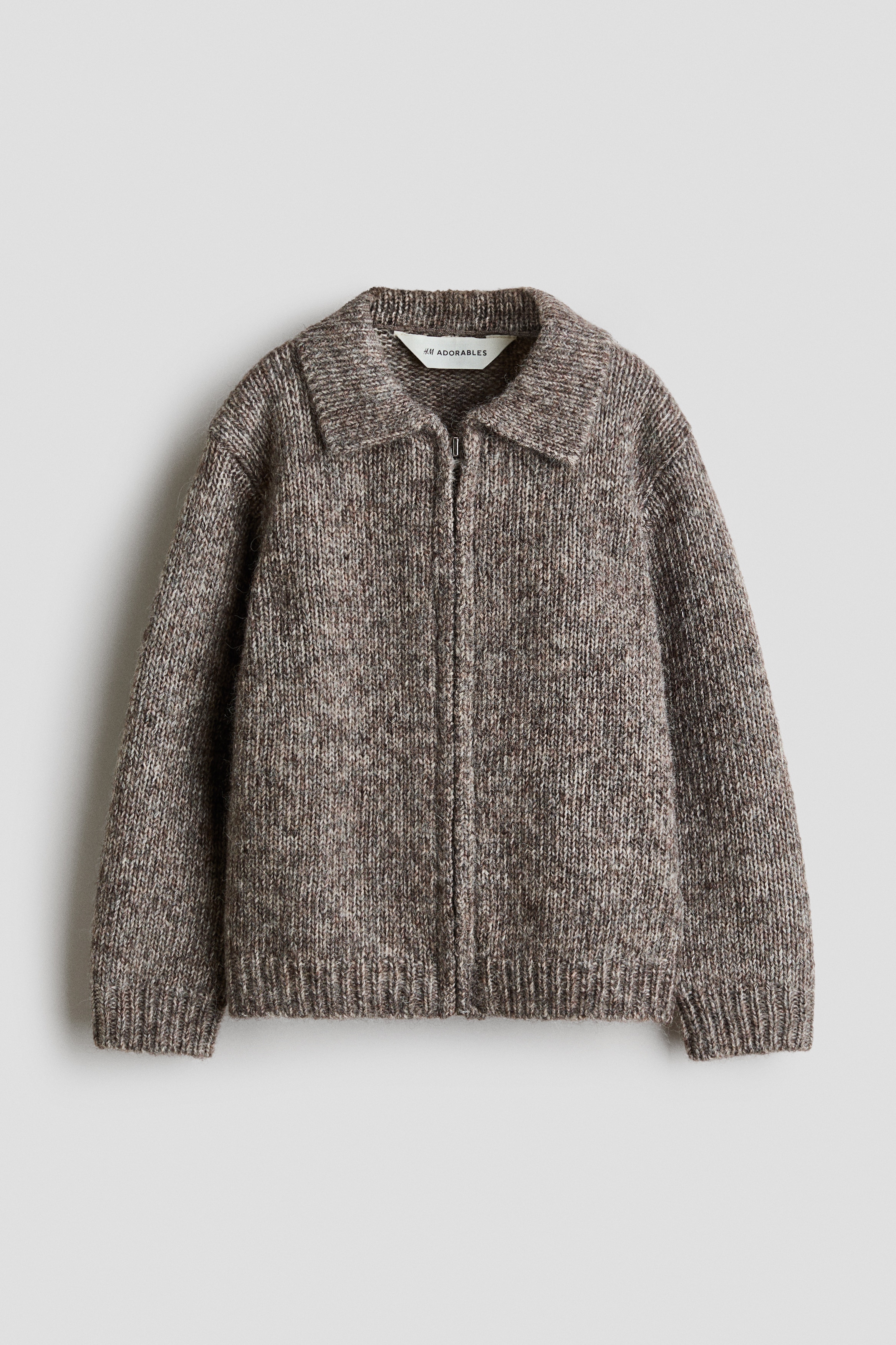 A grey-brown melange knit cardigan is shown from the front, featuring a classic collar, dropped shoulders, and ribbed cuffs. The cardigan is being worn unzipped, layering over a white polo shirt to showcase its soft, textured fabric and relaxed fit.