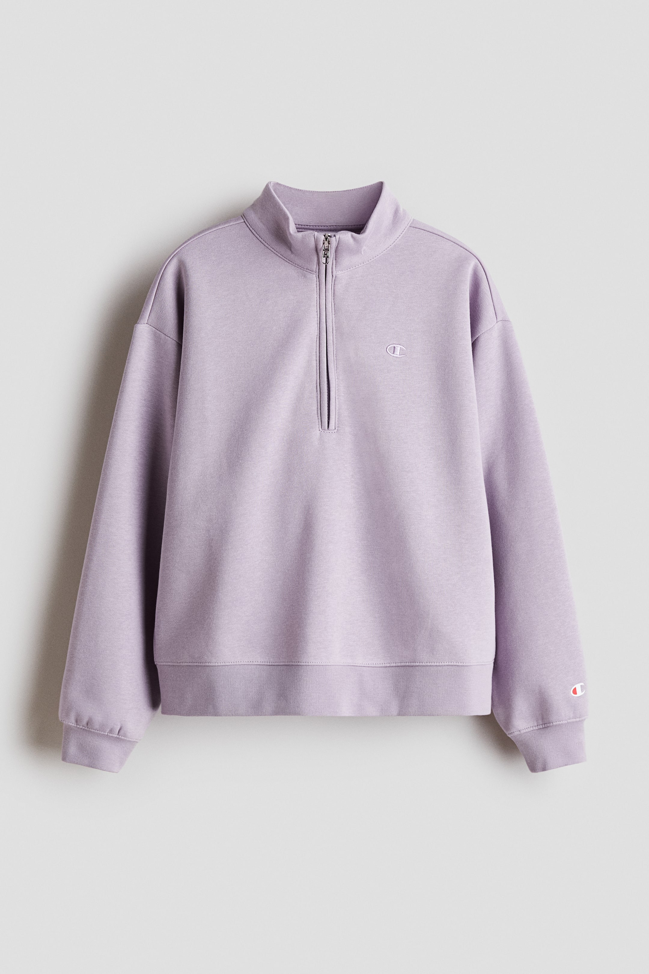 Näytä suurempi kuva: Vaalean violetti neljännesvetoketjullinen collegepaita näytetään edestä, ja siinä on pystykaulus ja hopeansävyinen vetoketju. Se on suunniteltu pitkähihainen, ribatut hihansuut ja ribattu helma, kun taas pieni kirjailtu logo on näkyvissä vasemmassa rinnassa ja pieni paikkalogo on vasemmassa hihassa.