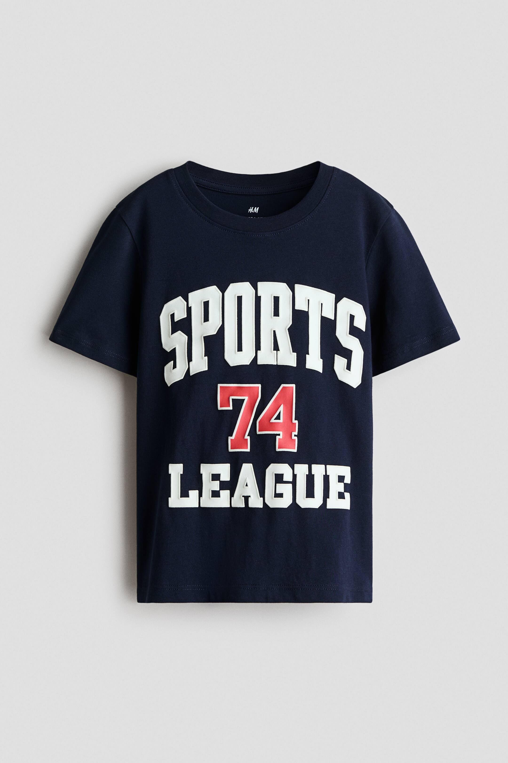 View larger image: A navy blue short-sleeved t-shirt is lying flat, facing forward, featuring a white, slightly raised "SPORTS" graphic above a red, slightly raised "74" graphic, which is above a white, slightly raised "LEAGUE" graphic on the front.