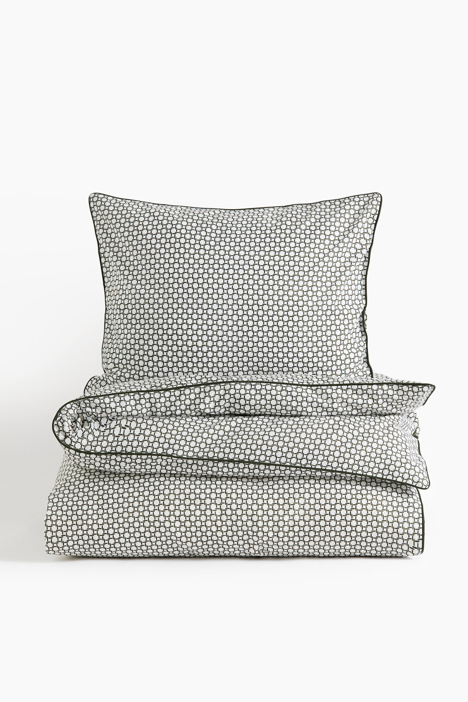 A bedding set consisting of an upright pillowcase and a folded duvet cover is displaying a repeating black-and-white geometric grid pattern. Both items are facing front and are featuring thin, dark green piped trim along the edges.