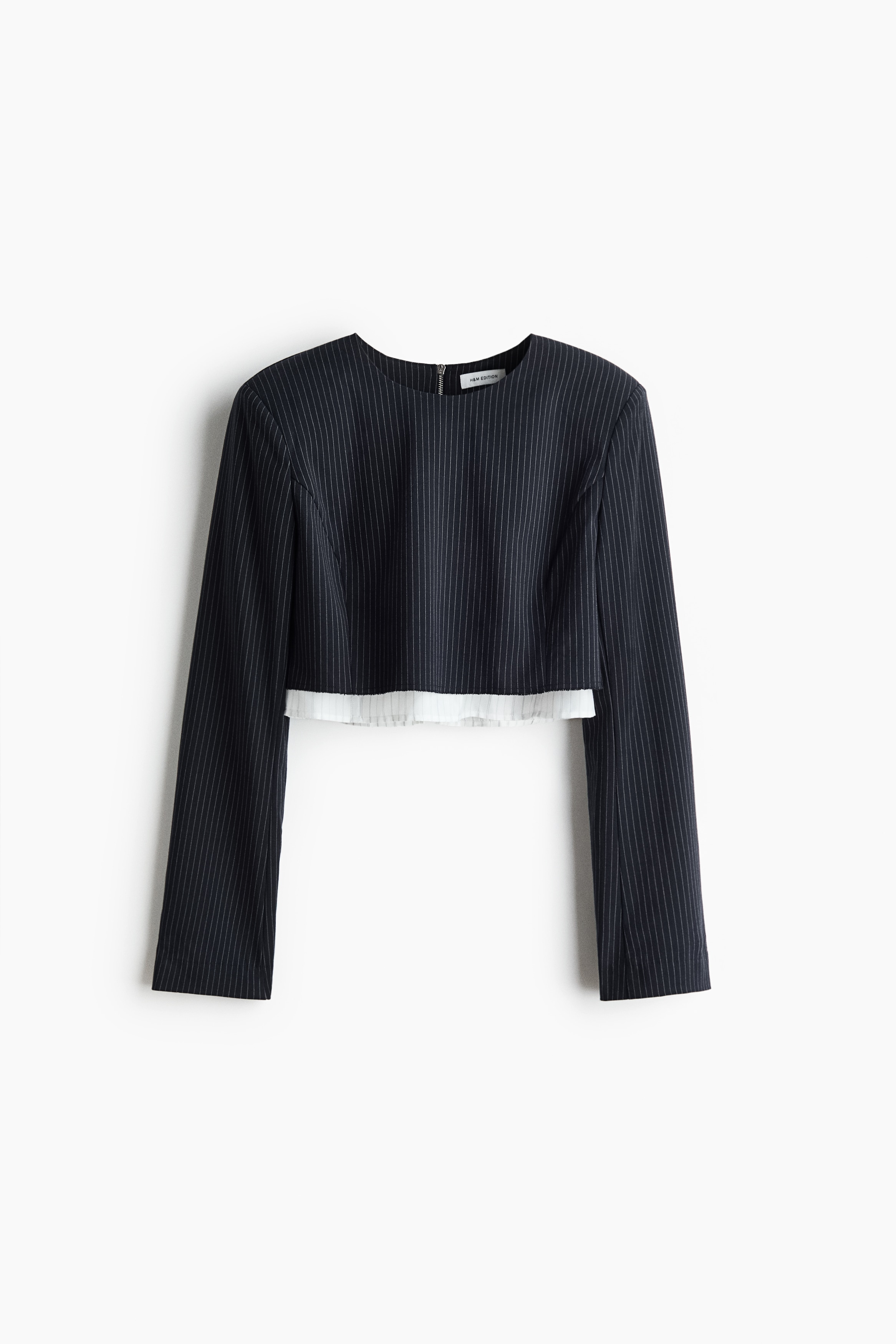 Un haut court Ã  manches longues Ã  fines rayures, avec un col rond et des Ã©paules structurÃ©es, est portÃ© par le mannequin. Le haut prÃ©sente un design superposÃ© avec une sous-couche blanche dÃ©passant de lâourlet, portÃ© avec un pantalon assorti Ã  fines rayures.