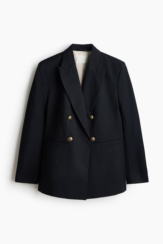 A black double-breasted blazer is shown from the front, featuring peak lapels, four embossed gold-toned metal buttons, and two horizontal welt pockets. The structured jacket has a light-coloured interior lining visible at the collar and long, straight sleeves. - 1