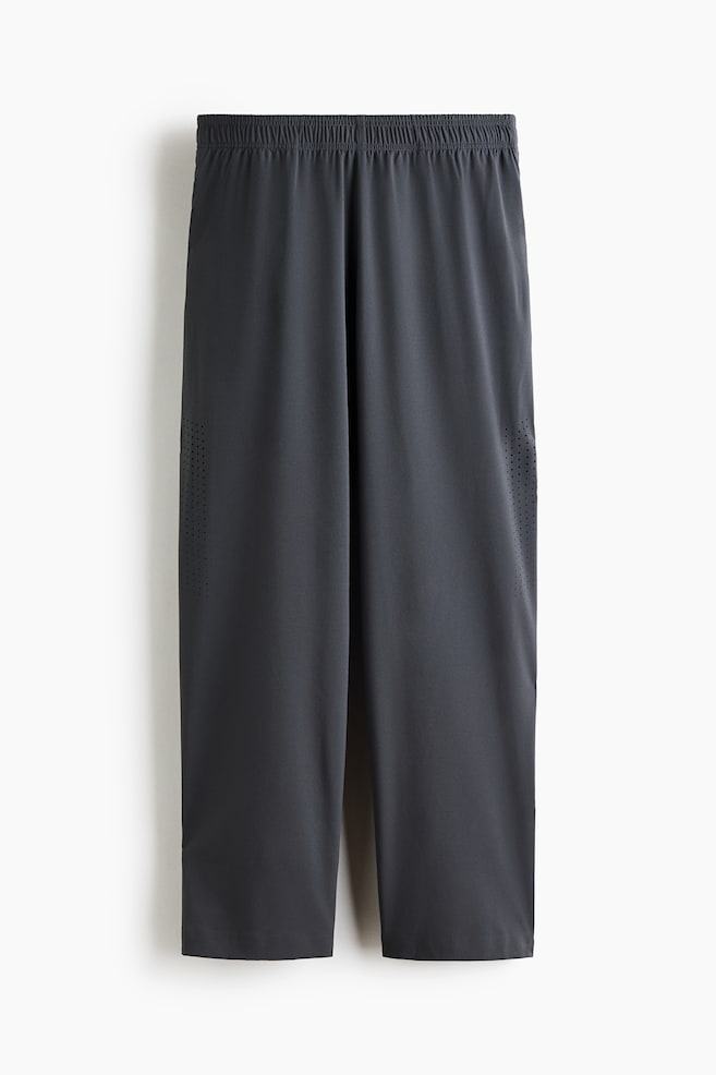 Dark grey athletic trousers are hanging in a front-facing view, featuring an elasticated waistband and a relaxed, straight-leg fit. The trousers display vertical bands of laser-cut perforated ventilation details along the outer sides of each leg. - 1