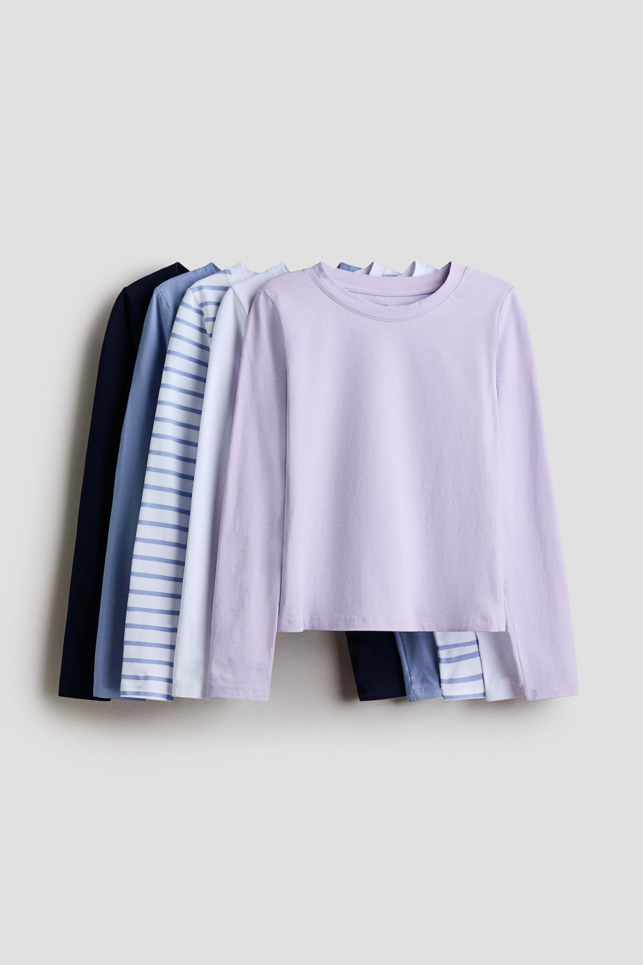 查看大圖: 柔軟純棉針織衫，圓領和長袖設計，正面展示它們的設計。淡紫色上衣位於前景，背後可見層疊的白色和藍色條紋上衣、淡藍色上衣和海軍藍上衣。