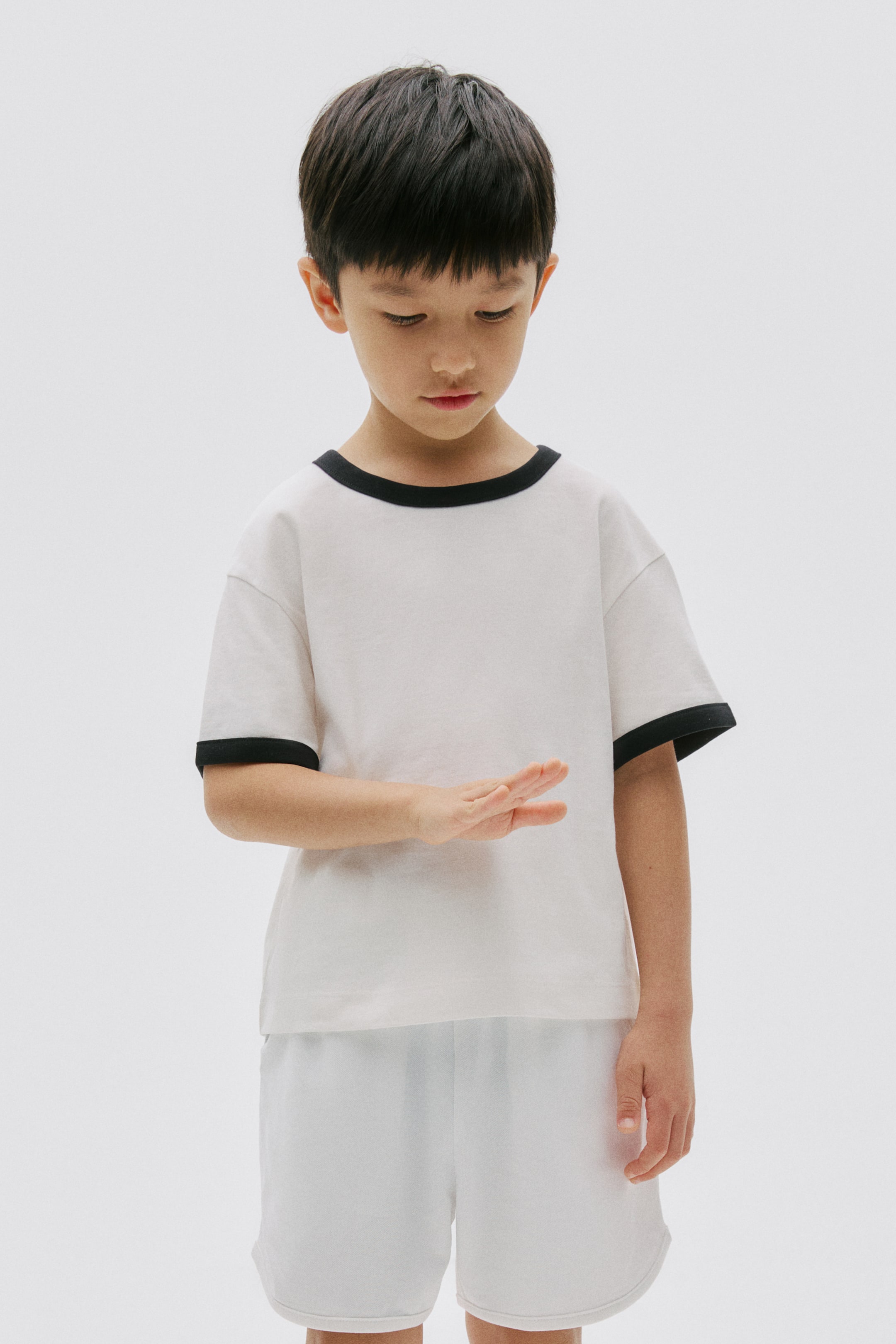 View larger image: An off-white short-sleeved t-shirt with black trim on its round neck and sleeve cuffs is coordinating with white loose-fitting shorts, forming a two-piece set.