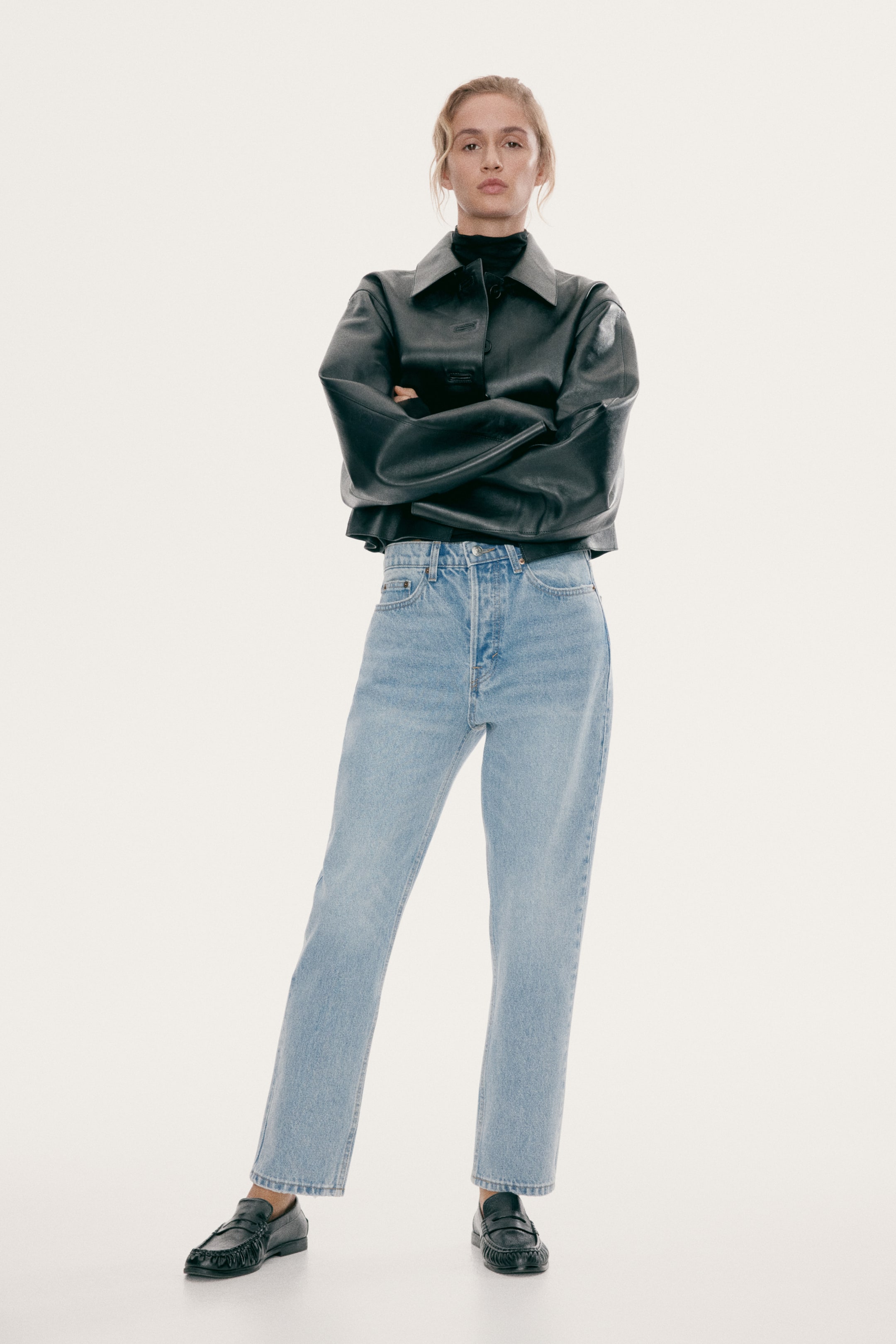 Visa större bild: Ljusvättade, högmidjade blå denimjeans med rak passform bärs av modellen. Jeansen stylas med en kort svart läderjacka, en svart polotröja och svarta loafers.