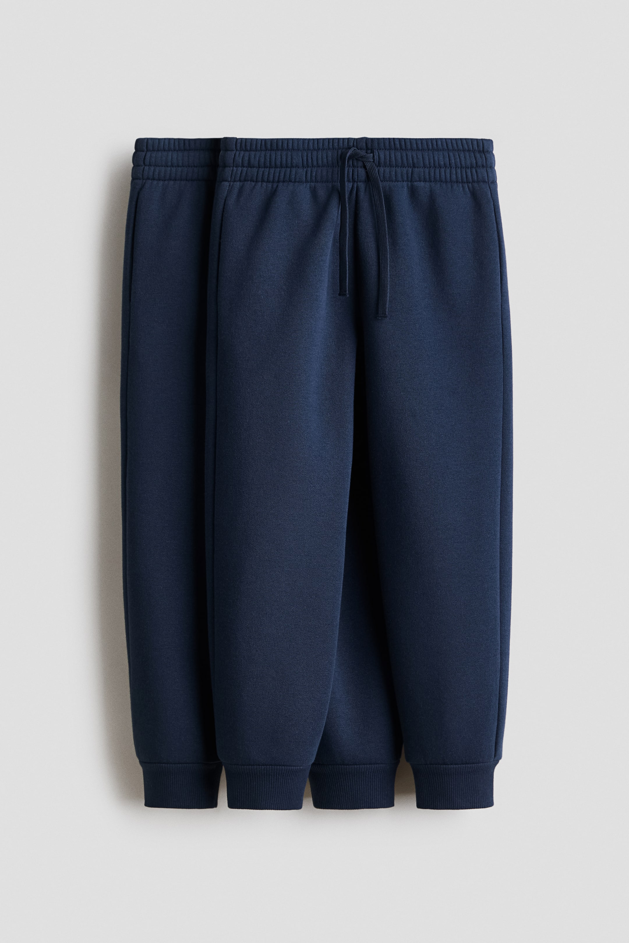 View larger image: The front of the navy joggers features an elasticated waist with a visible drawstring. The joggers feature side pockets and ribbed trims at the hems, all crafted from a smooth sweatshirt fabric.