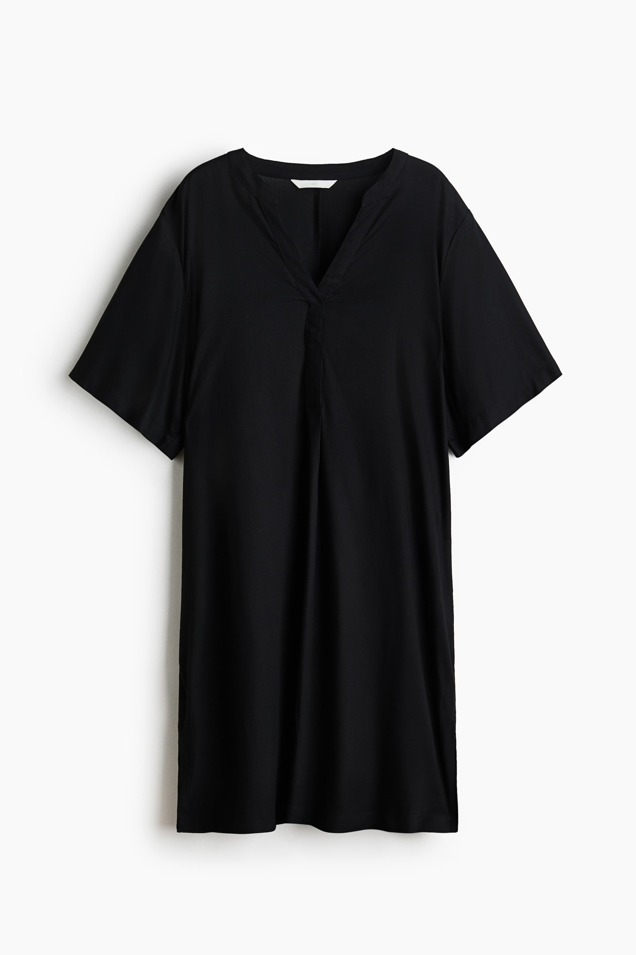 View larger image: A black knee-length tunic dress is showcased front-facing, featuring a banded collar and a V-shaped opening at the front. It's crafted with a relaxed fit, subtly dropped shoulders, and short sleeves, finished with a straight-cut hem that includes slits on each side.