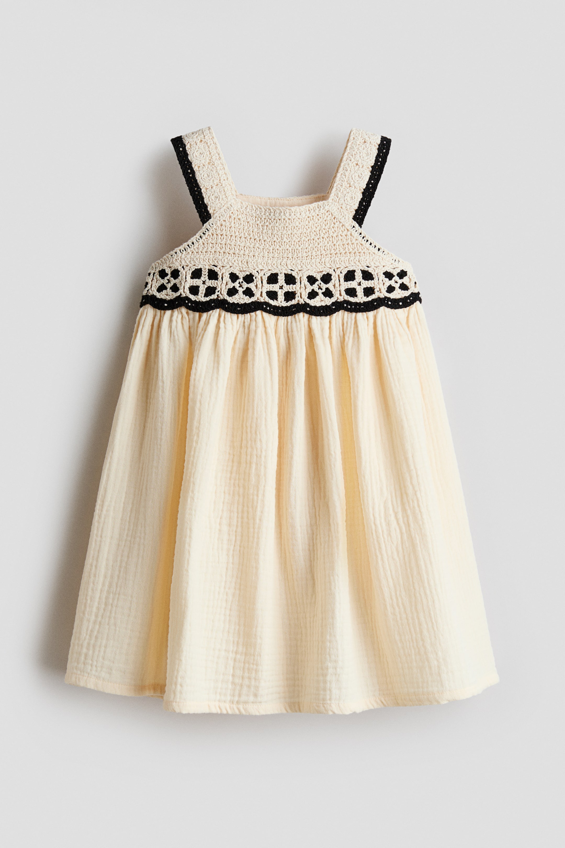 View larger image: The dress features a cream-colored crocheted bodice with wide straps, trimmed with black along the edges. A black openwork crochet band accents the waistline, where it meets a gathered cream-colored crinkled fabric skirt.