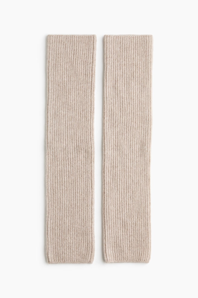A pair of light beige leg warmers in a rib-knit wool blend are laid flat side by side, showcasing their vertical ribbed texture and straight, tubular design from the front. - 1