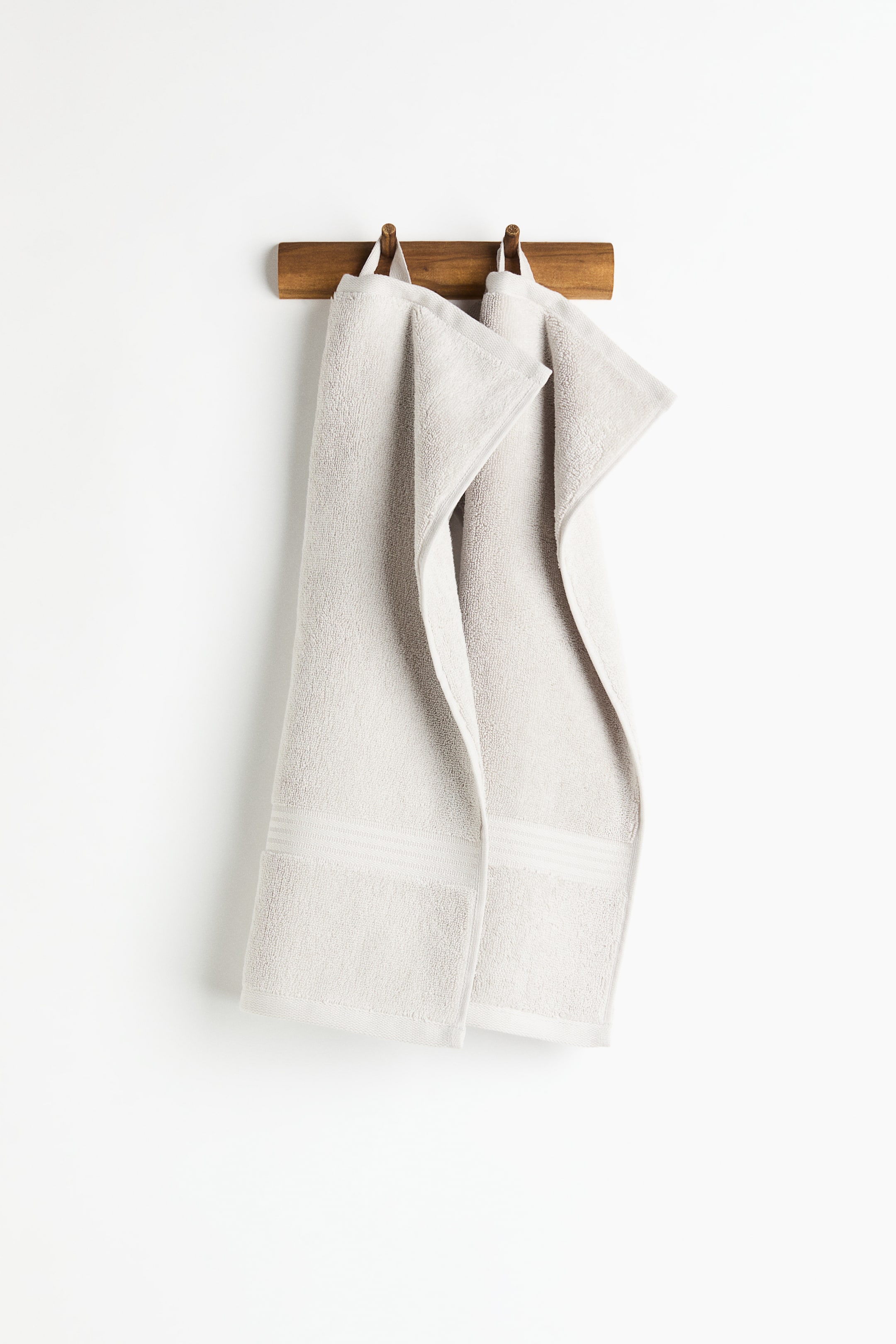View larger image: Two light grey terry cloth towels are hanging from a wooden rack by their white loops, each showcasing a decorative woven band of horizontal stripes near the bottom edge.