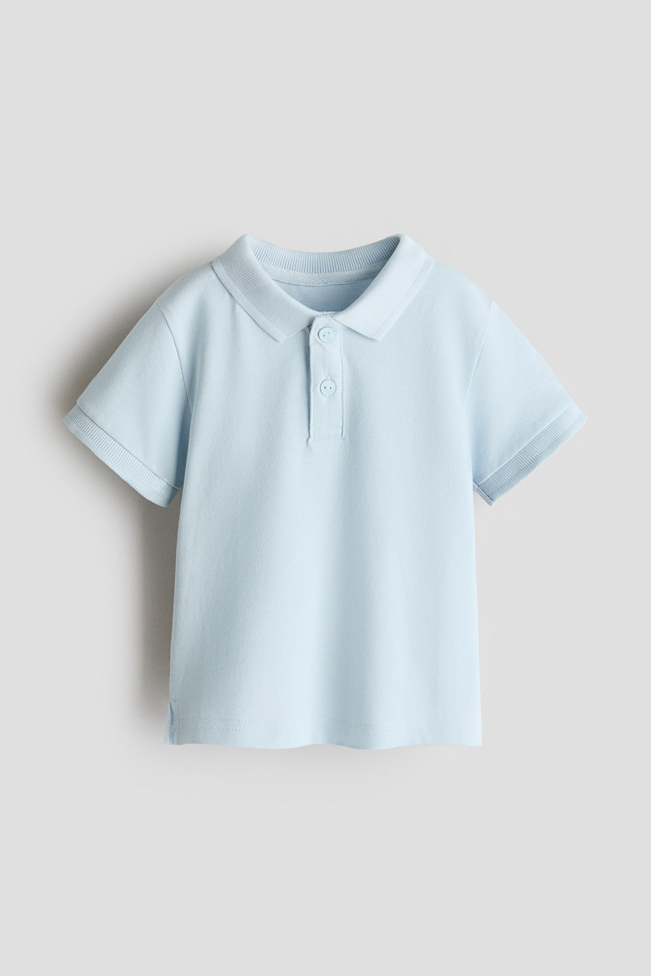 View larger image: A light blue polo shirt is showcased with its front view, highlighting a ribbed collar, a two-button placket, and short sleeves with ribbed cuffs. The shirt features a textured pique knit fabric and a straight hem with small side slits.