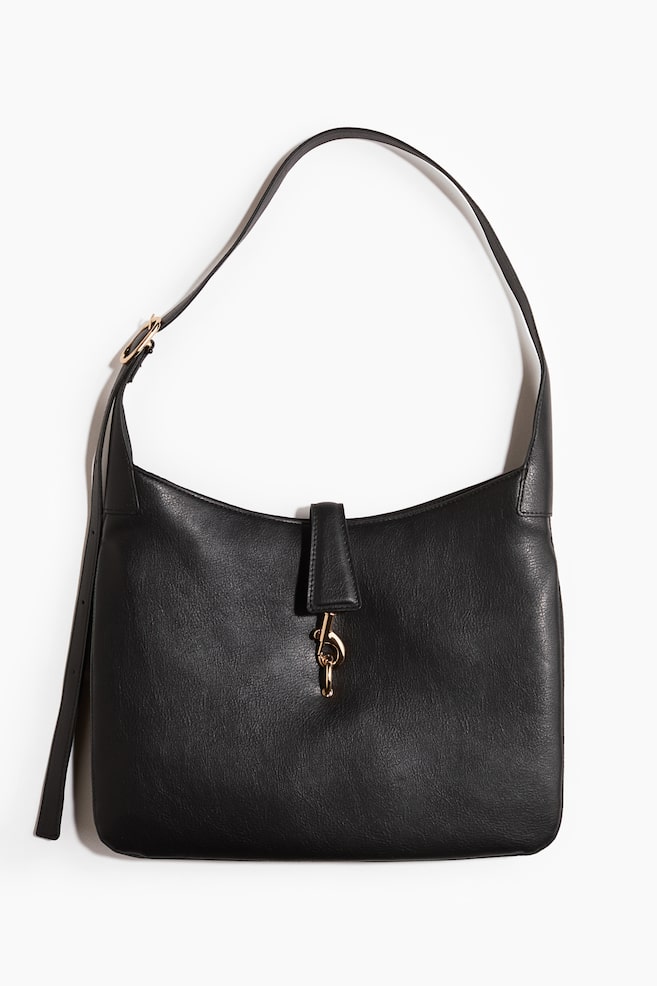 A black handbag is shown front-facing, featuring a single shoulder strap with a gold-toned buckle. It showcases a grained texture and a flap closure secured by a gold-toned dog clip. - 1