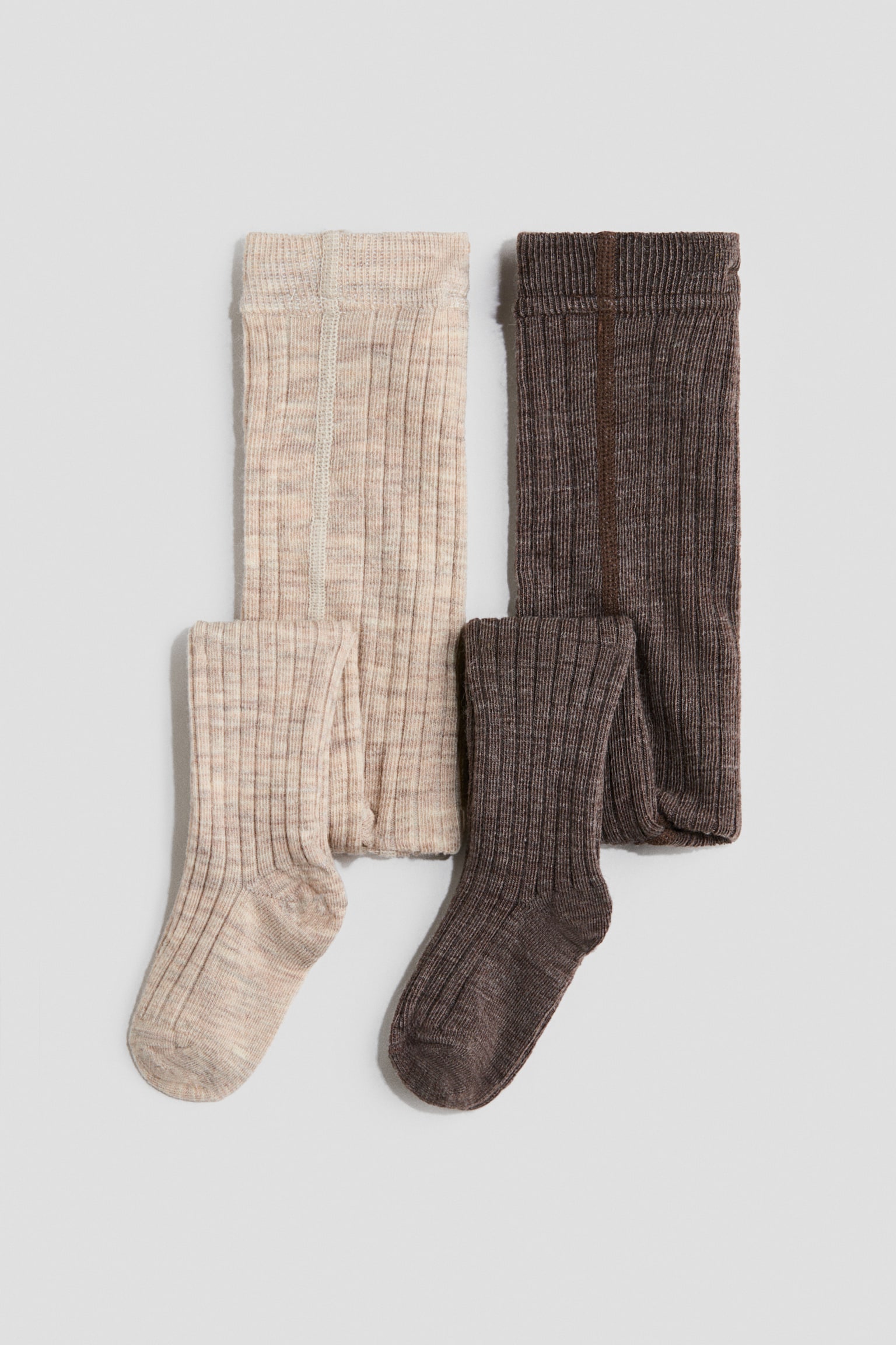 Two pairs of ribbed knit tights are lying flat in a front-facing view, featuring one light beige marl pair and one dark brown marl pair. Both pairs are displaying a vertical ribbed texture, an elasticated waistband, and one leg folded forward to show the foot shape.