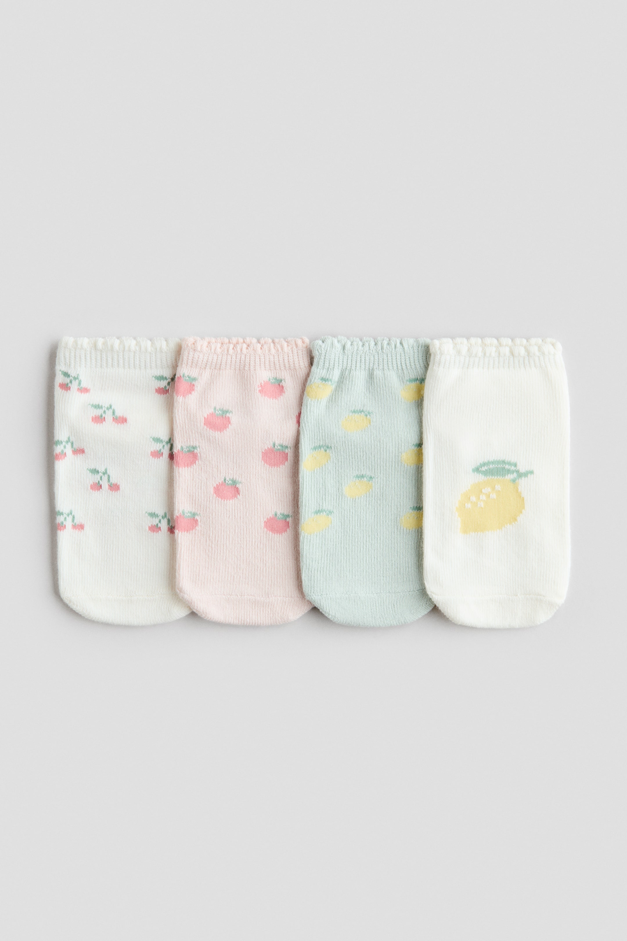 View larger image: Four shaftless socks are showcased side-by-side, facing front, each exhibiting a fine-knit texture and scalloped, elasticated tops. The socks flaunt unique fruit patterns: white adorned with cherries, light pink embellished with strawberries, light blue featuring small lemons, and white with a prominent single lemon.