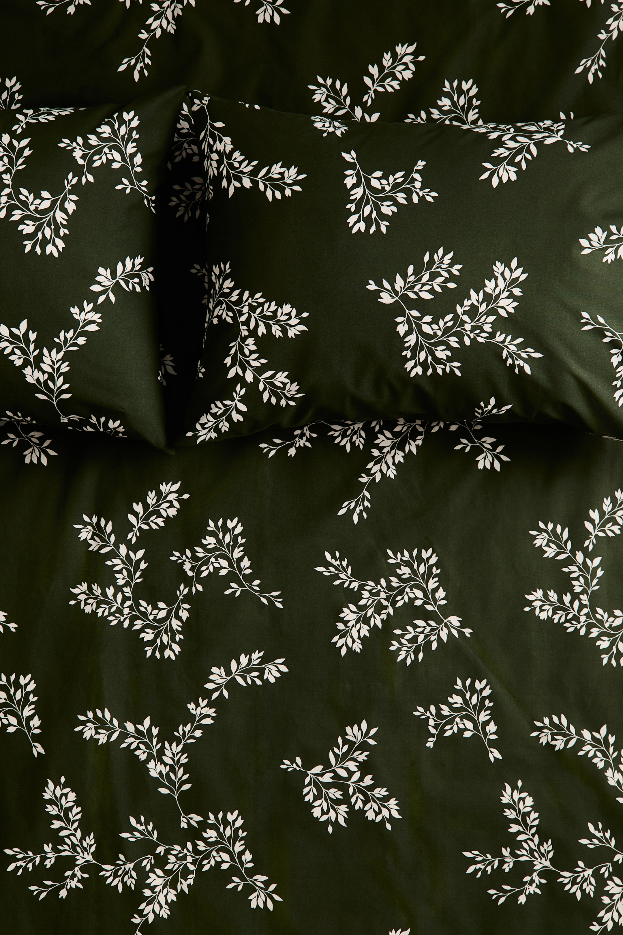 View larger image: A dark green bedding set featuring a white botanical pattern of delicate leafy branches is shown from a top-down perspective. Two matching pillowcases are resting flat at the top of the duvet cover, displaying the uniform print across the entire set.