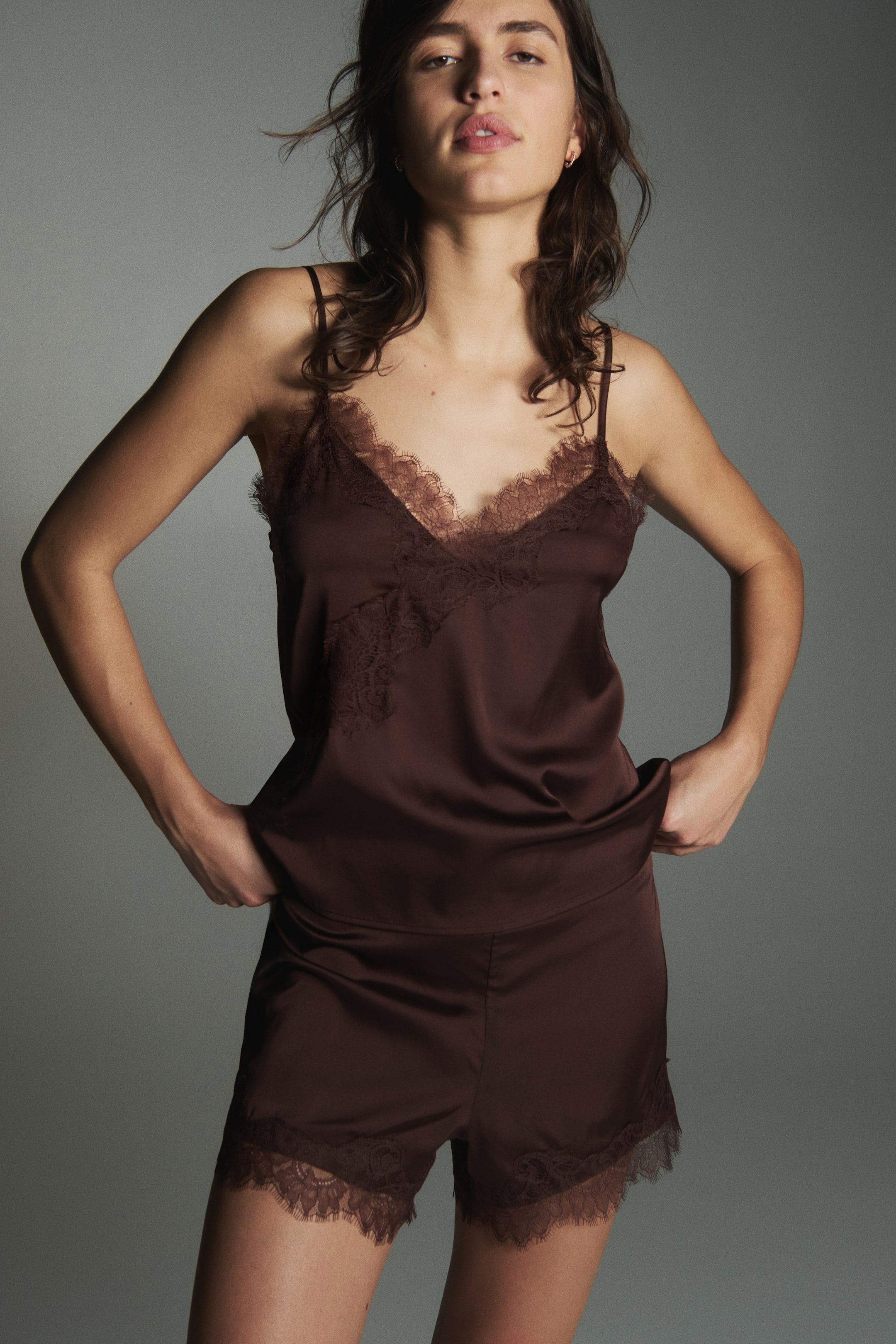 View larger image: A brown satin camisole and shorts set is presented facing front, featuring a V-neck camisole with spaghetti straps and matching brown lace trimming the neckline and extending down the front. The coordinating shorts also feature matching brown lace along the hems.