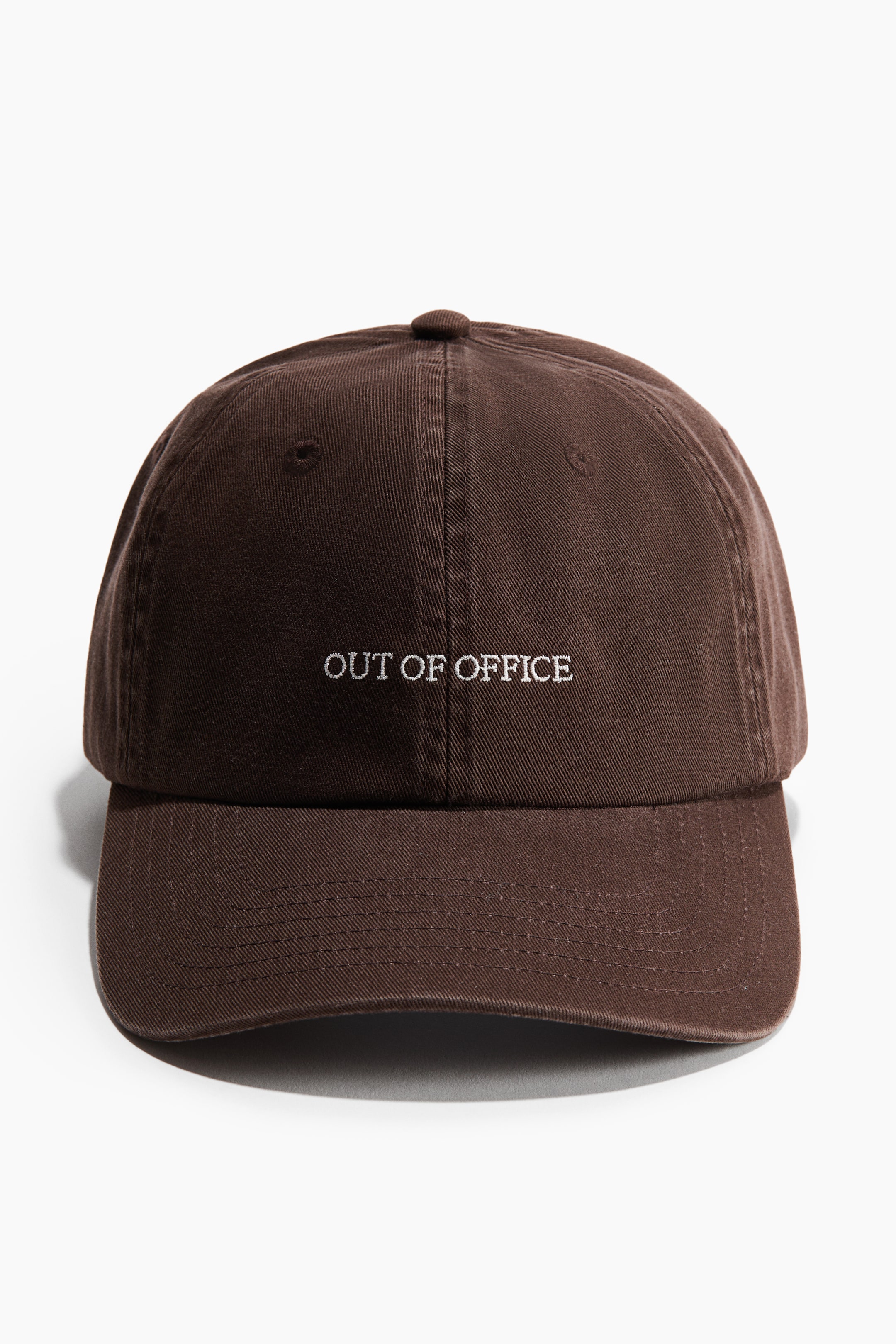 Grösseres Bild ansehen: Eine braune Baumwoll-Twill-Kappe ist nach vorne gerichtet, mit weißem gesticktem Text "OUT OF OFFICE" auf der Vorderseite, einem gebogenen Schirm, einer sechsteiligen Konstruktion und Belüftungsösen.