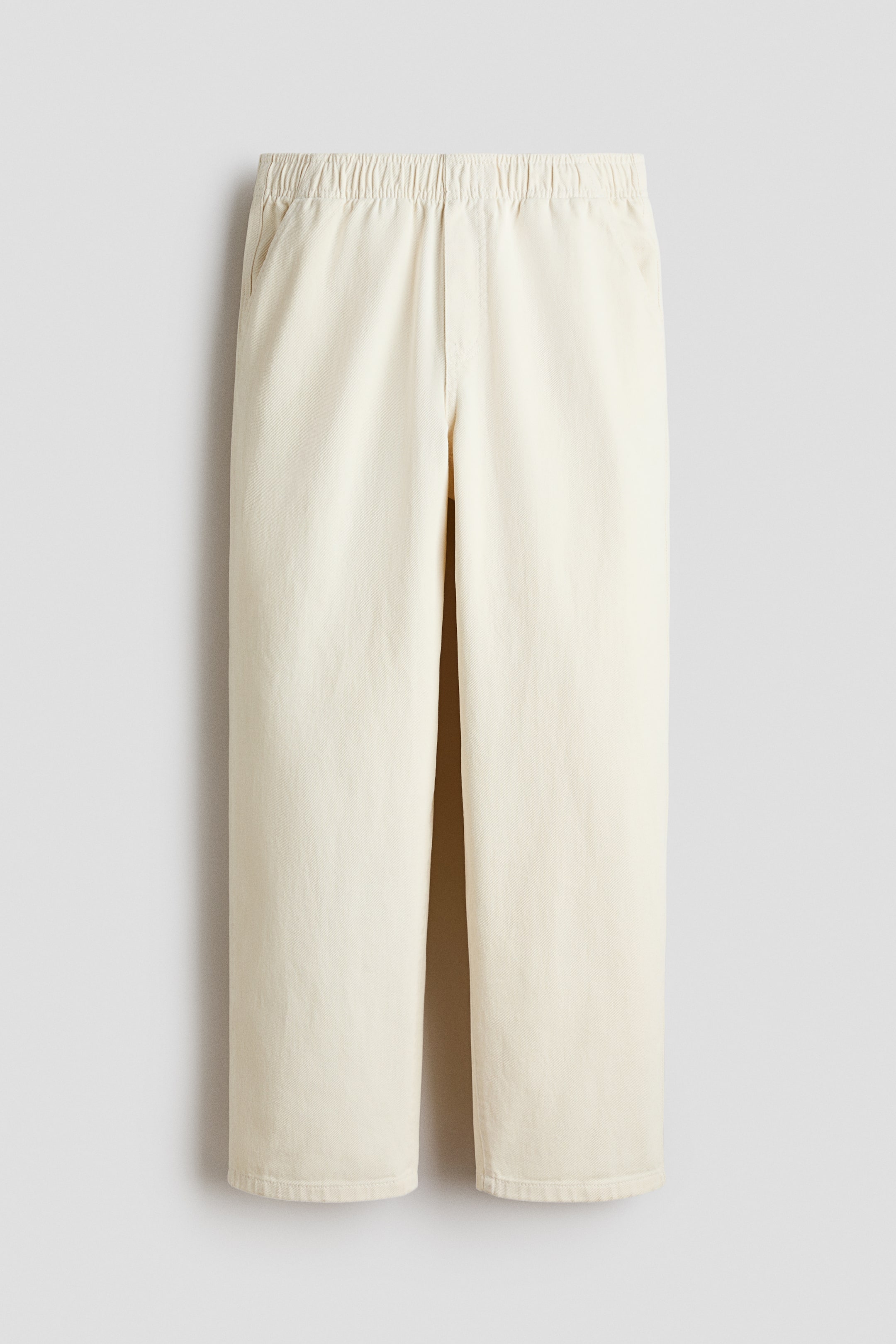 View larger image: Light beige joggers crafted from soft cotton twill are showcased in a front view. They feature an elastic waistband, a faux fly, and diagonal side pockets. The design offers a relaxed fit through the hips and thighs with slightly tapered legs.