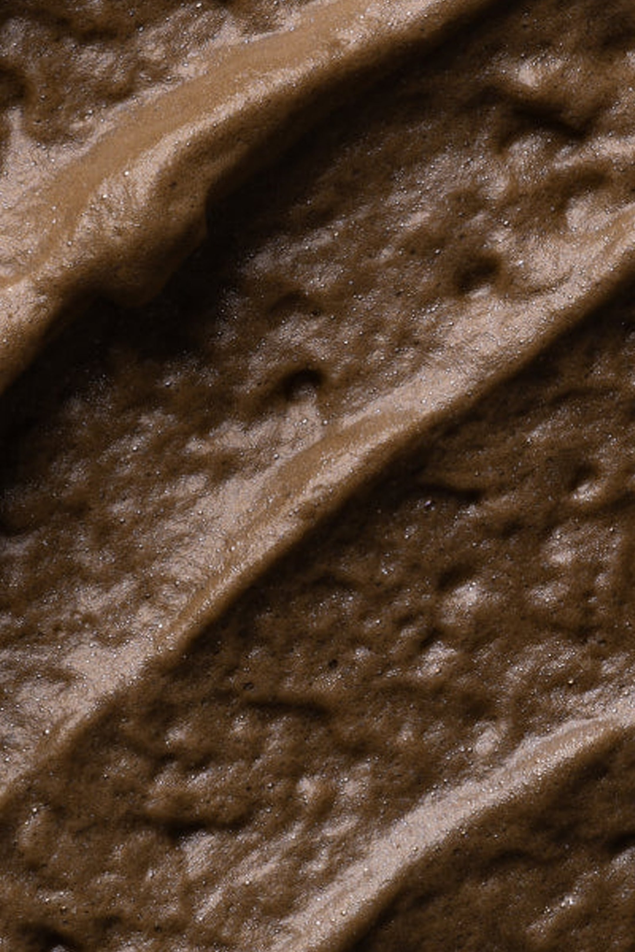 Visa större bild: En brun, trögflytande substans fyller ramen, med en texturerad yta med diagonala åsar och dalar. Produkten uppvisar olika nyanser av brunt, en lätt glans på dess upphöjda områden och små, synliga partiklar som bidrar till dess ojämna textur.