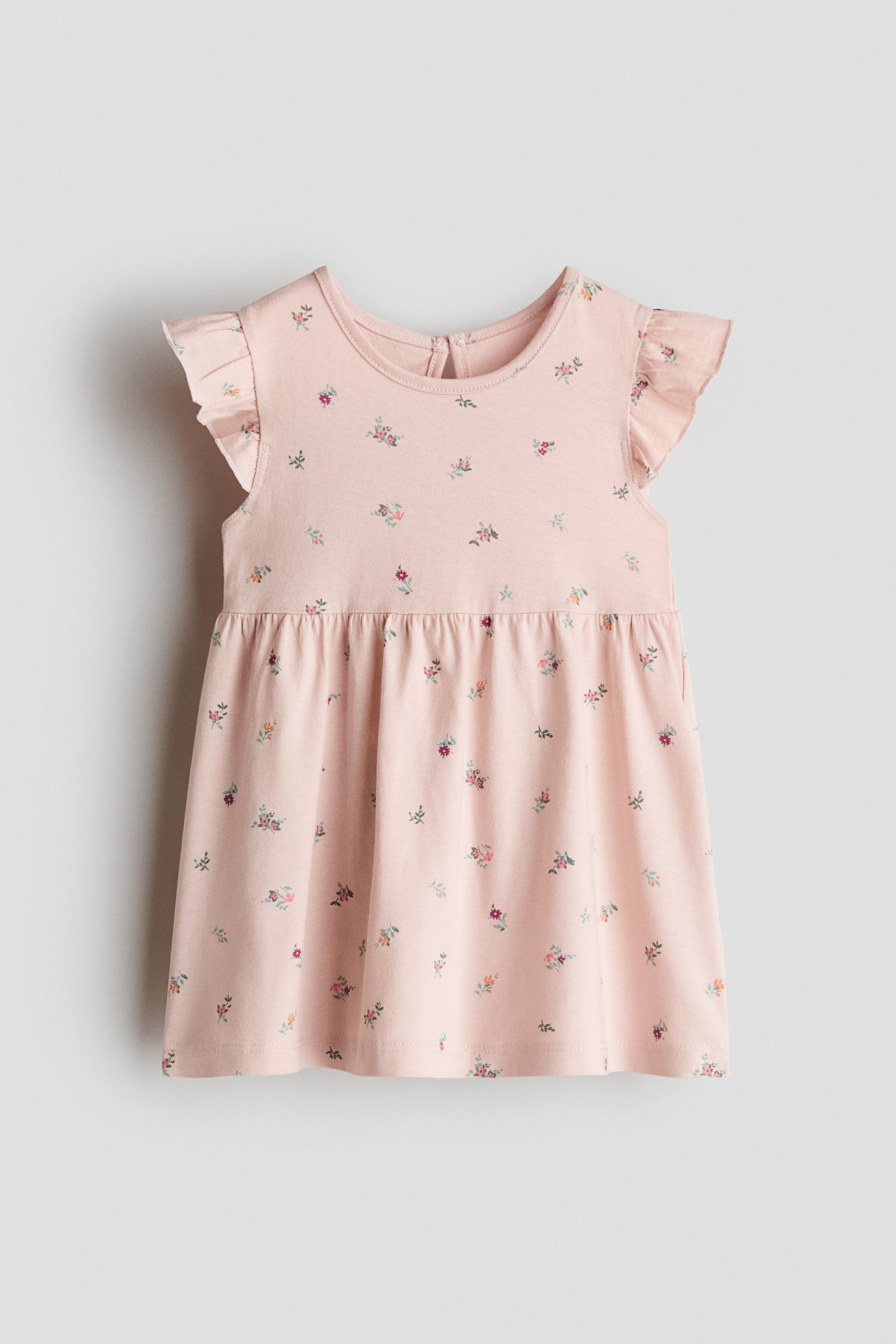 View larger image: Presenting the front view of a pink cotton jersey dress, adorned with a delicate floral print. It features a round neckline and flutter sleeves, designed with gathers at the waist and a flared skirt. The dress also includes a keyhole opening with a button at the back neckline.
