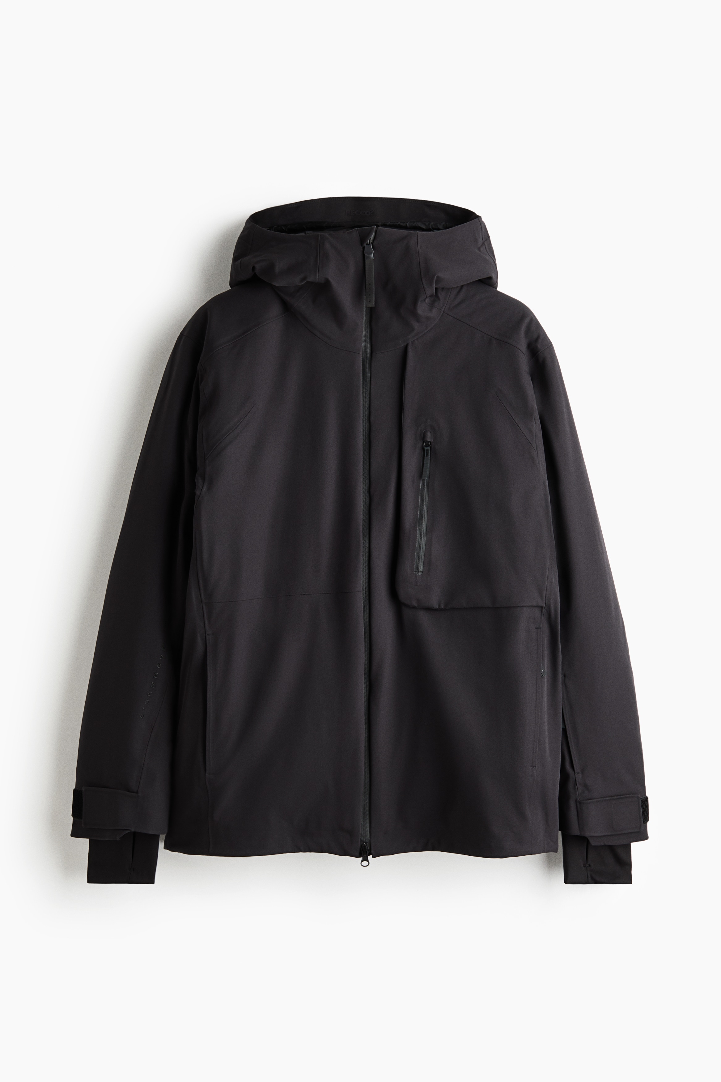 Eine schwarze technische Jacke mit Kapuze, FrontreiÃverschluss, vertikaler Brusttasche mit ReiÃverschluss und verstellbaren ÃrmelbÃ¼ndchen wird vom Model getragen. Die Jacke ist mit einer passenden schwarzen Hose, Handschuhen und Skibrille auf der Stirn des Models kombiniert.
