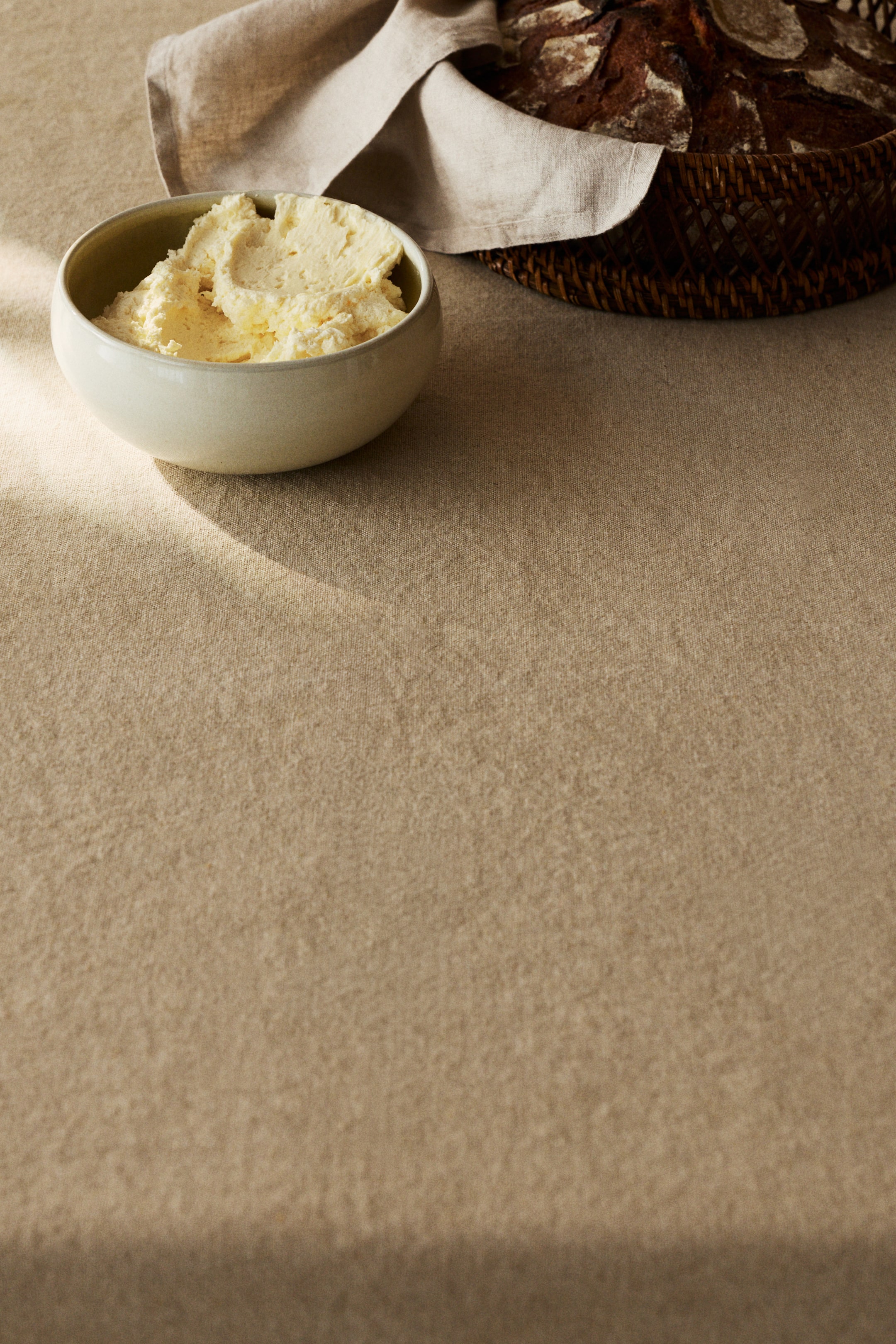 Ver imagem maior: Uma tigela de cerâmica de cor creme clara com uma borda interior verde pálida contém manteiga suave de um amarelo pálido. A manteiga apresenta picos e redemoinhos visíveis, enchendo a tigela quase até à borda e inclinando-se ligeiramente para a esquerda.