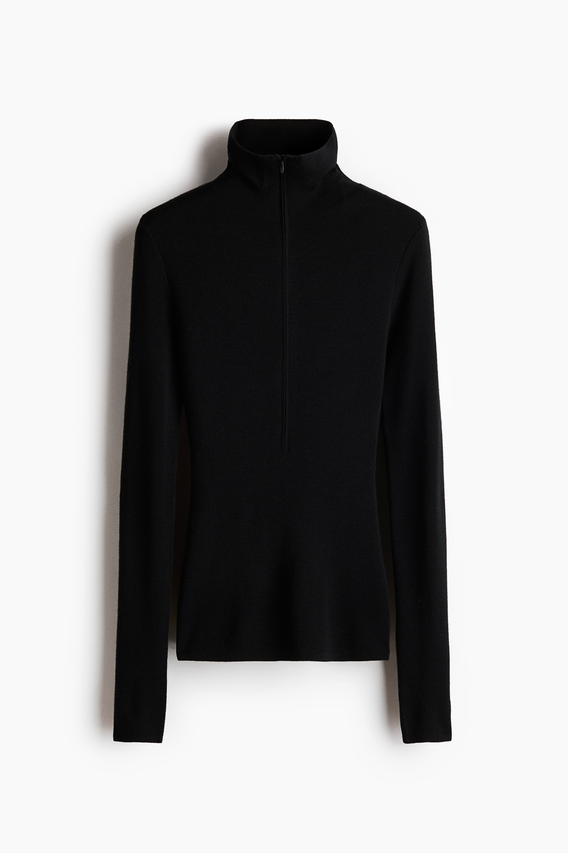 A black, fitted rib-knit merino wool top featuring a high neck with a small zip detail is being worn by the model. The close-up view highlights the close fit and fine texture of the collar.