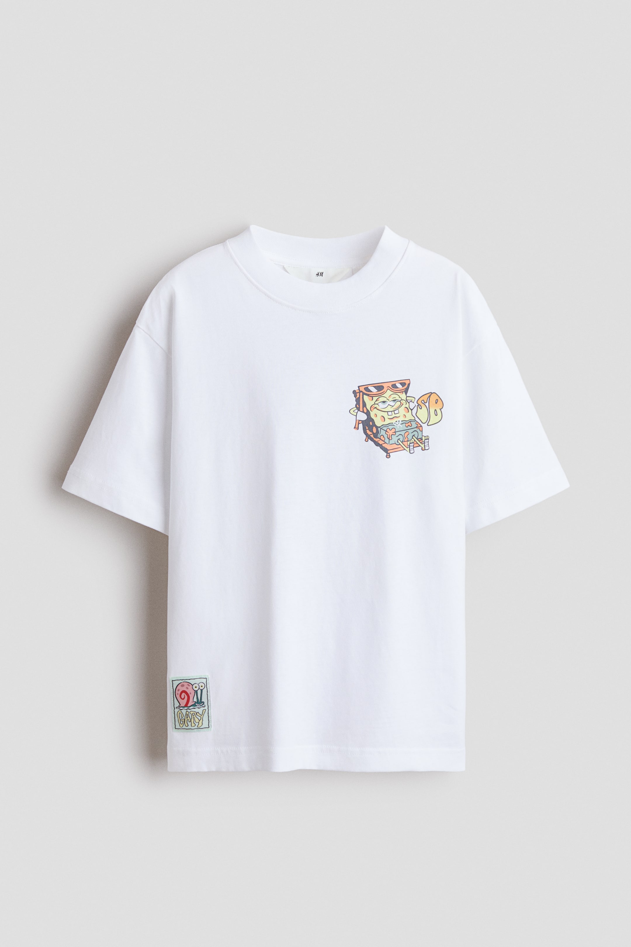 View larger image: The white t-shirt showcases its front, crafted from soft cotton jersey with a ribbed trim around the neckline. It features a loose fit with dropped shoulders. A colorful graphic print of SpongeBob SquarePants playing a keyboard appears on the left chest, while a small rectangular patch depicting Gary the snail is visible on the bottom left.
