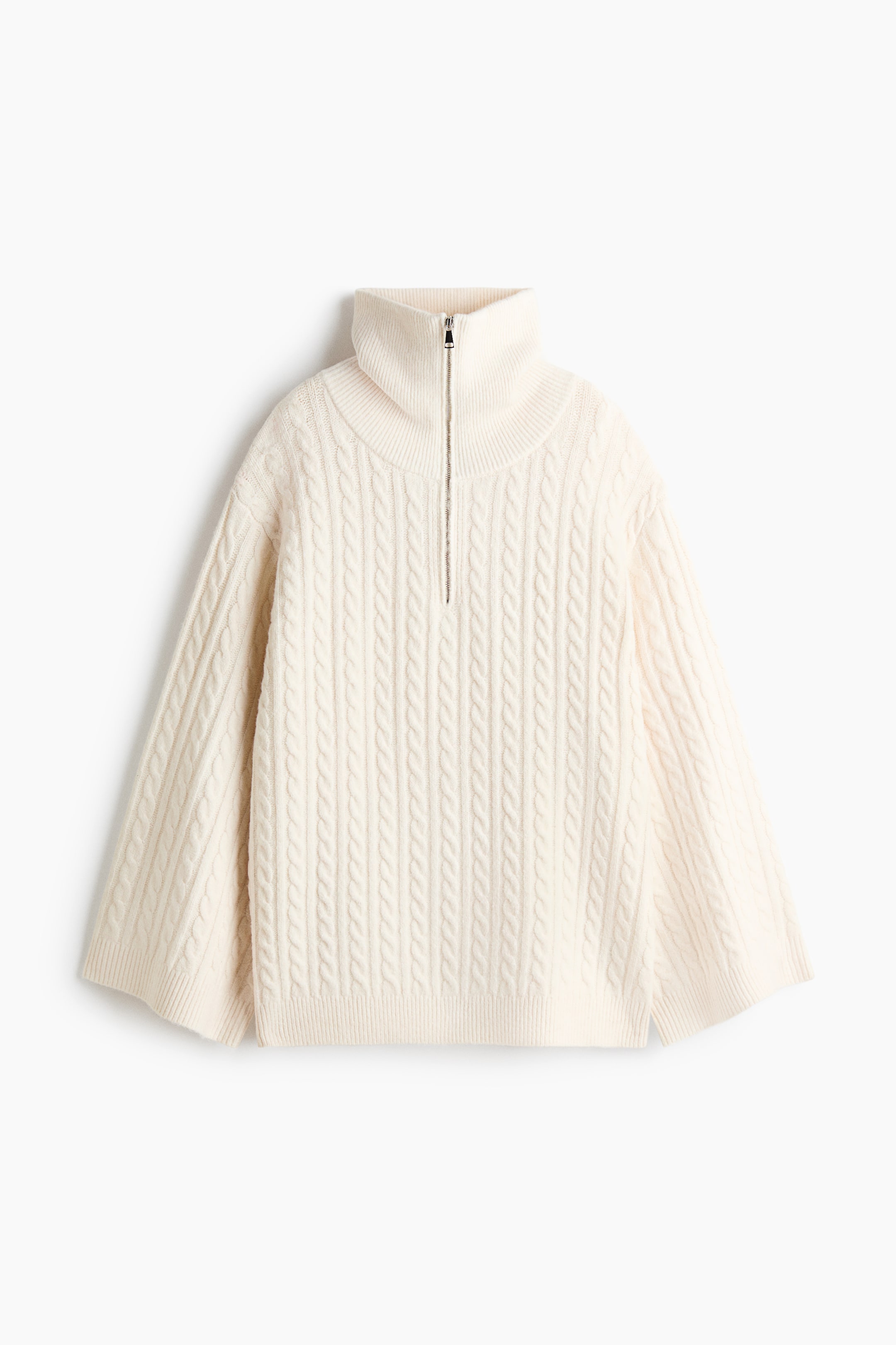Größeres Bild anzeigen: Ein cremefarbener Zopfpullover wird von vorne gezeigt und verfügt über einen hohen gerippten Kragen mit einem silbernen Half-Zip-Verschluss. Der Pullover ist in lockerer Passform mit weiten, ausgestellten Ärmeln und einem gerippten Saum dargestellt.
