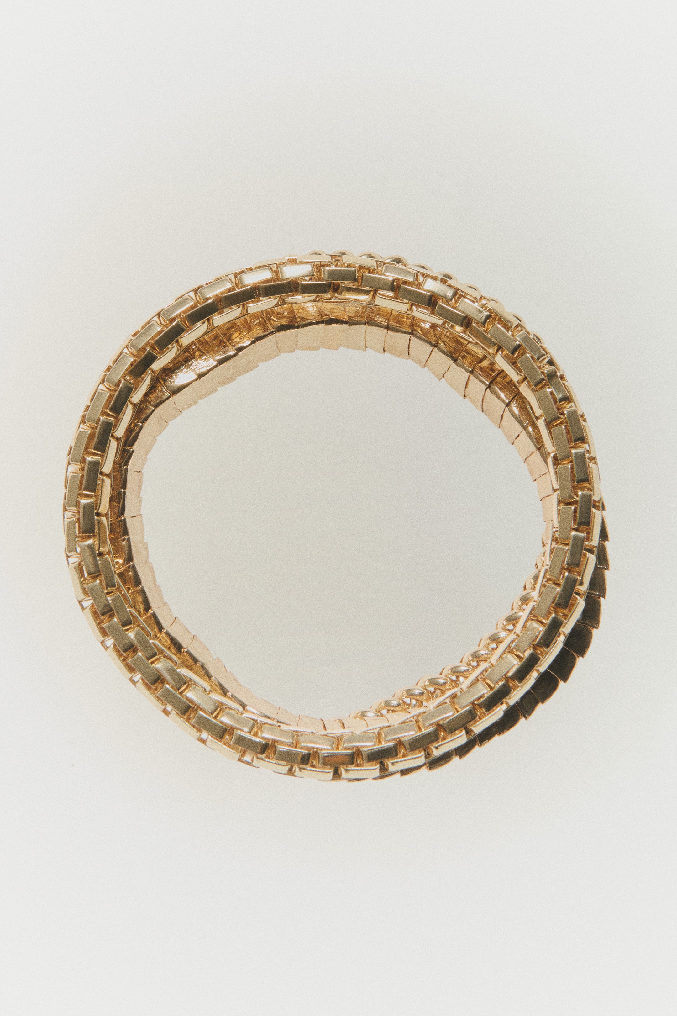 Agrandir l'image: Des bracelets en métal doré au design segmenté en blocs apparaissent disposés en un ensemble circulaire superposé, orientés de face. Les bracelets mettent en valeur des maillons rectangulaires polis et imbriqués qui forment un bracelet texturé et souple.