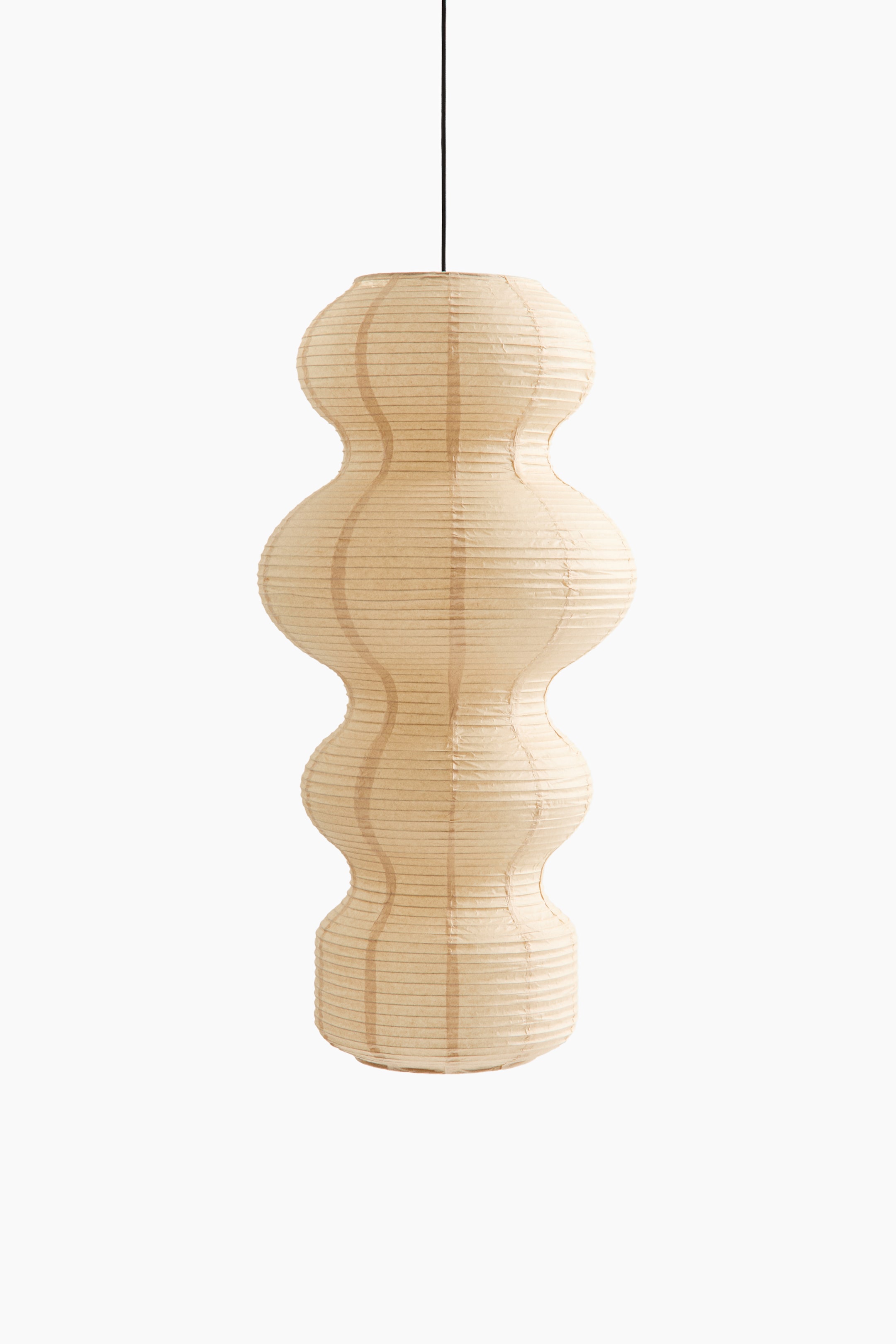 View larger image: A pendant lamp featuring a tall, sculptural rice paper shade in a light beige hue hangs from a thin black cord, shown from the front. The shade presents an undulating, multi-tiered silhouette defined by fine horizontal ribbing and vertical structural lines.