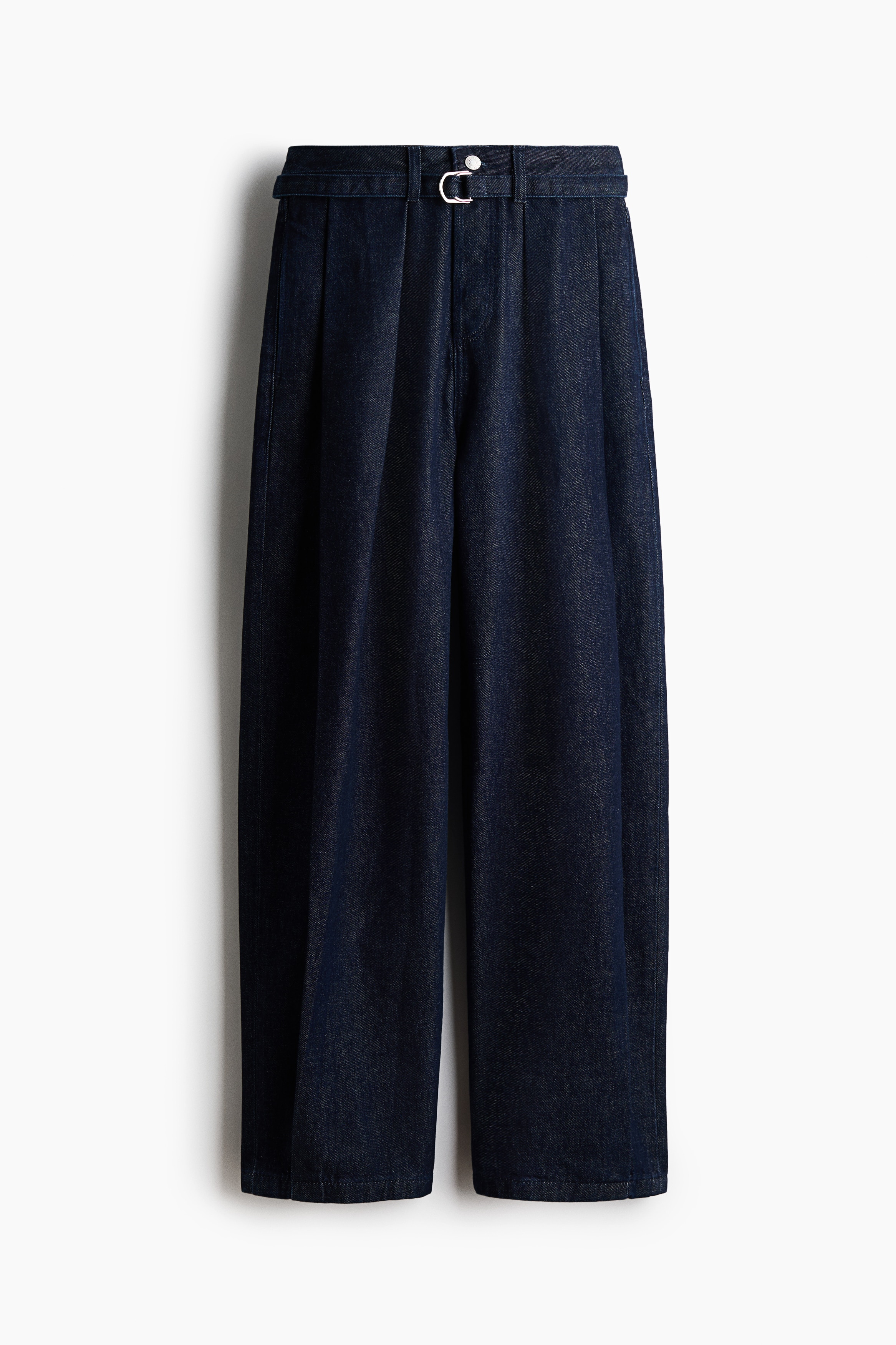 Jean en denim bleu foncÃ© prÃ©sentant des plis marquÃ©s sur lâavant et des jambes courbes et volumineuses, portÃ© par le mannequin. Ce pantalon taille haute est associÃ© Ã  une veste en cuir noire et Ã  des bottines noires Ã  bout pointu.
