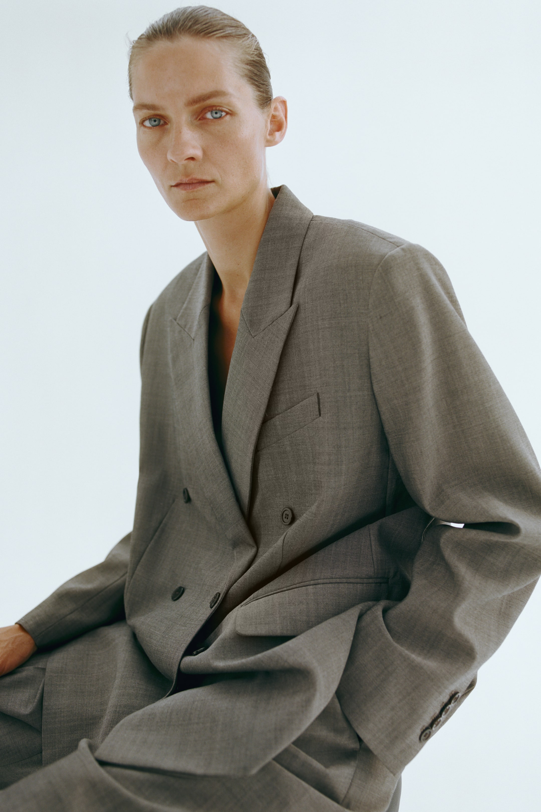 Ver imagen más grande: La modelo lleva puesto un blazer gris de corte oversize, cruzado y confeccionado en un tejido de mezcla de lana. El blazer presenta amplias solapas de pico, un bolsillo de pecho ribeteado y botones oscuros en el delantero.