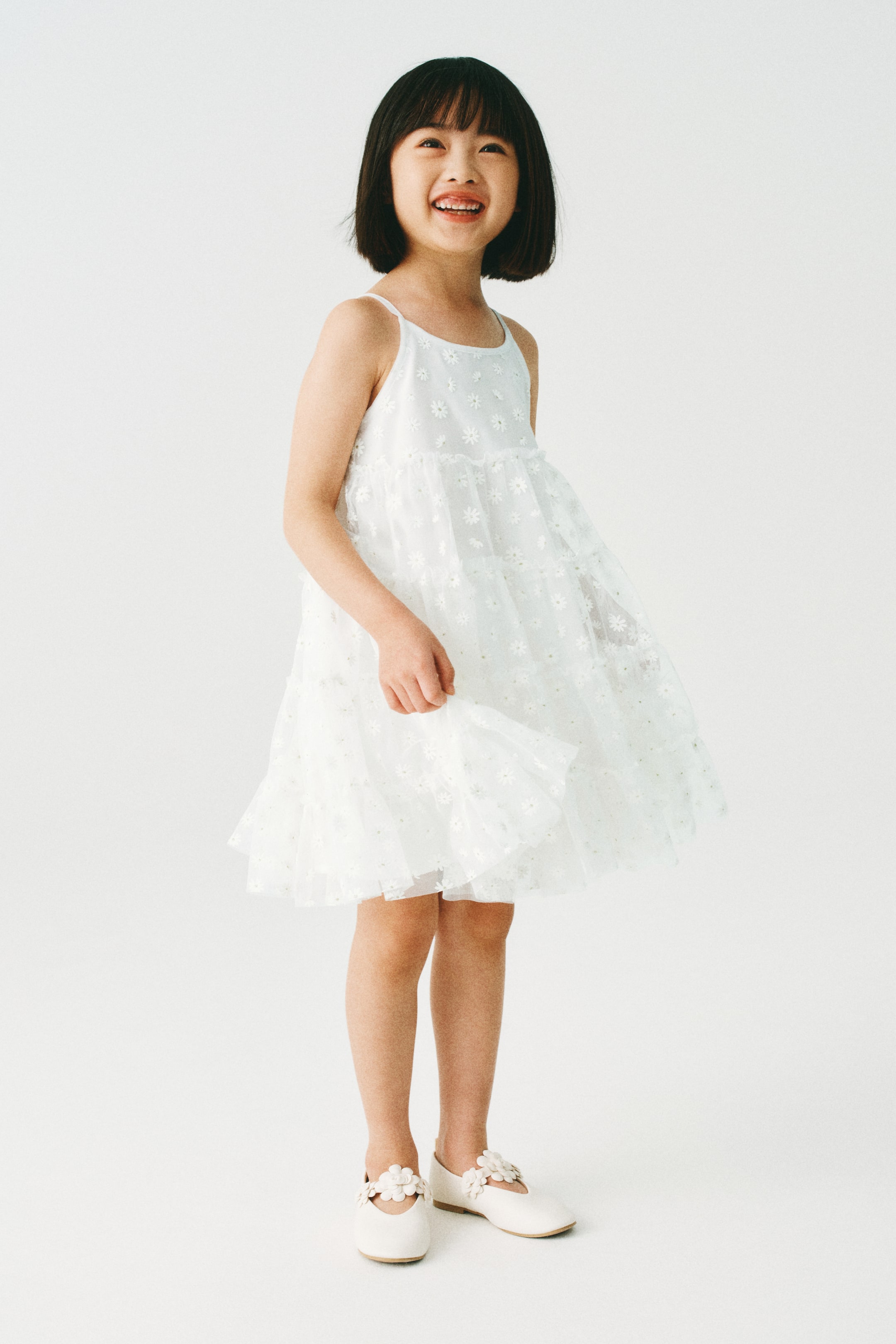 이미지 확대 보기: 스파게티 스트랩과 전체적으로 꽃 자수가 있는 밝은 색상의 티어드 드레스가 앞왼쪽 각도에서 시어 오버레이와 함께 전시되고 있습니다. 드레스는 발등 스트랩에 꽃 아플리케가 장식된 오프 화이트 메리 제인 플랫과 함께 스타일링되어 있습니다.