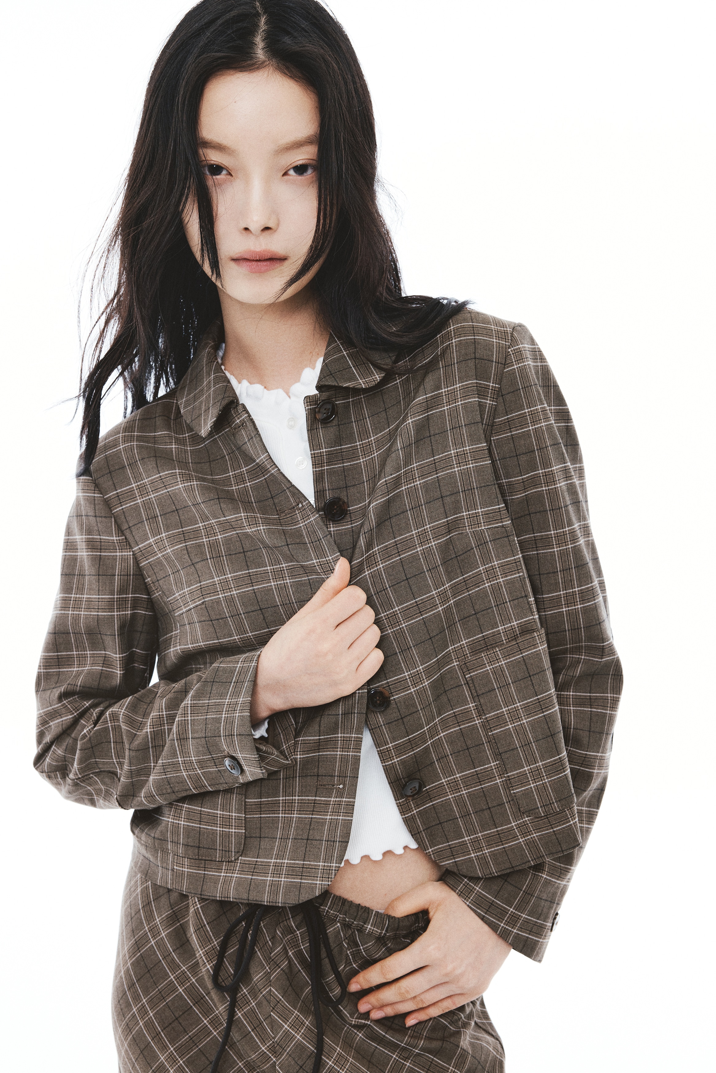 A brown plaid single-breasted blazer faces front, featuring a gently rounded collar, a five-button front closure, and two front patch pockets. The blazer has structured shoulders and long sleeves, with a cropped straight hem.