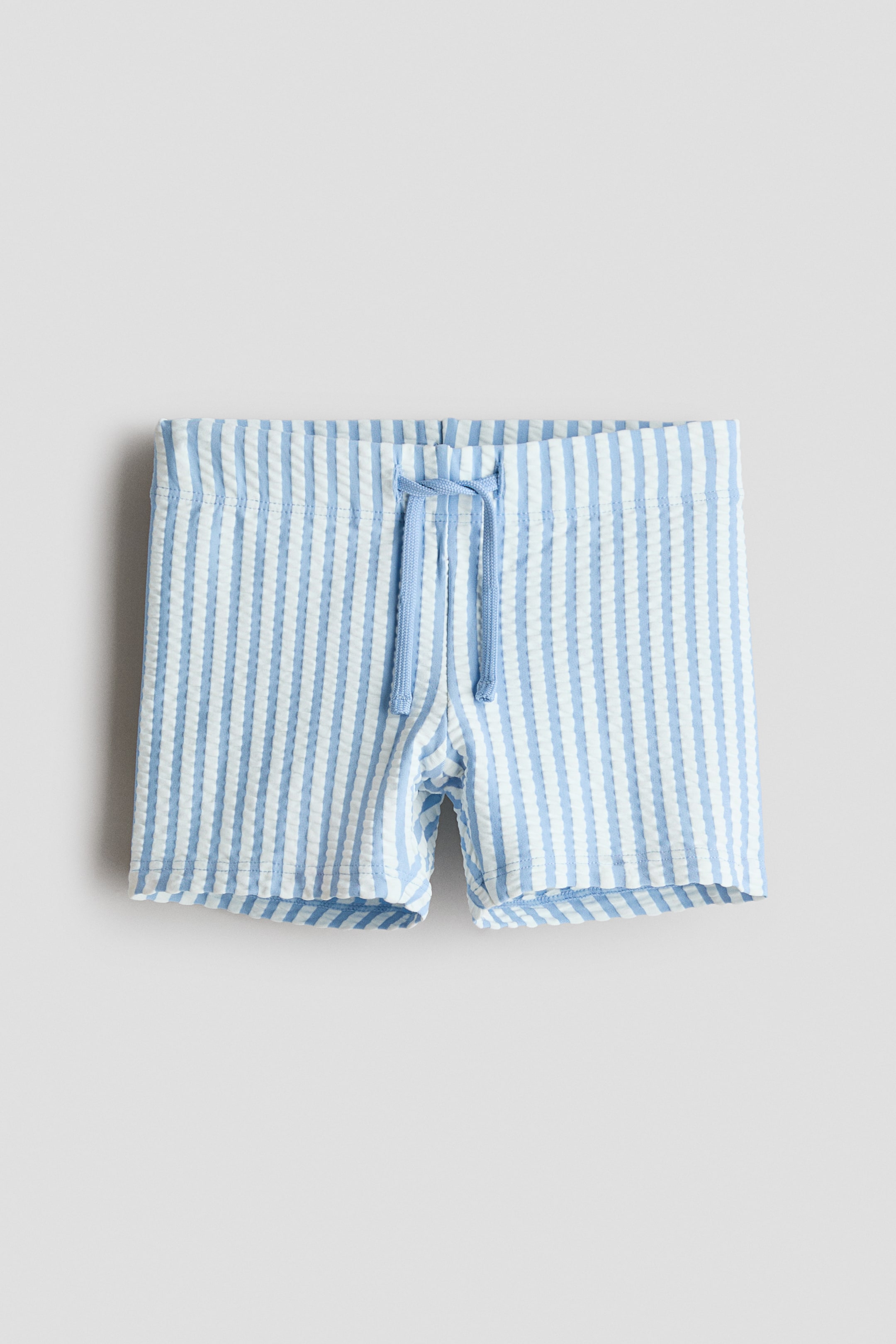 Преглед на по-голямо изображение: Банският костюм е показан отпред, с вертикални светлосини и бели райета от плат 'сирсъкър'. Те са проектирани с еластичен колан и светлосин шнур, завързан на панделка.