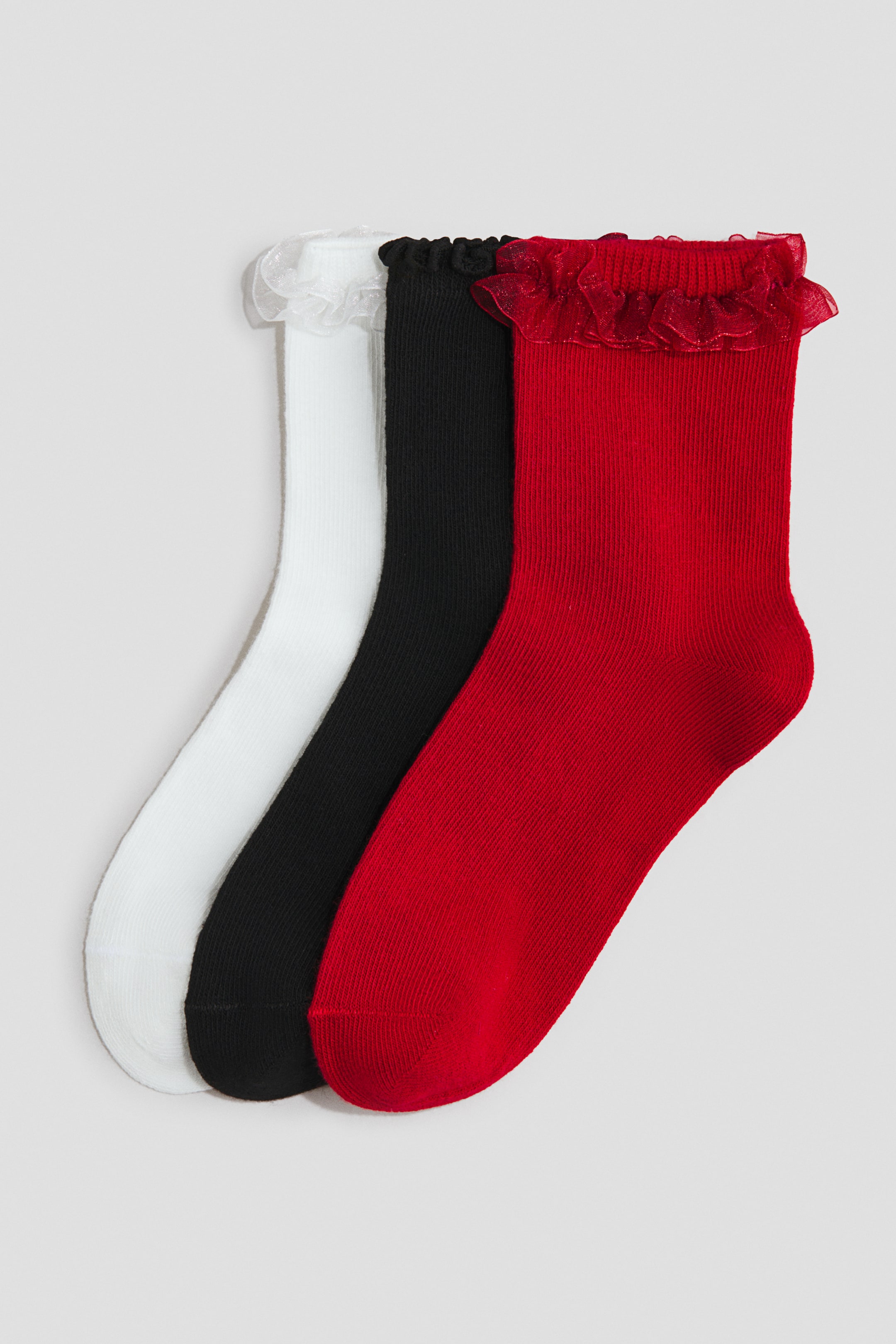 View larger image: Three socks are showcasing a fine-knit, ribbed texture in white, black, and red, each featuring an elasticated top with a shimmering frill trim.