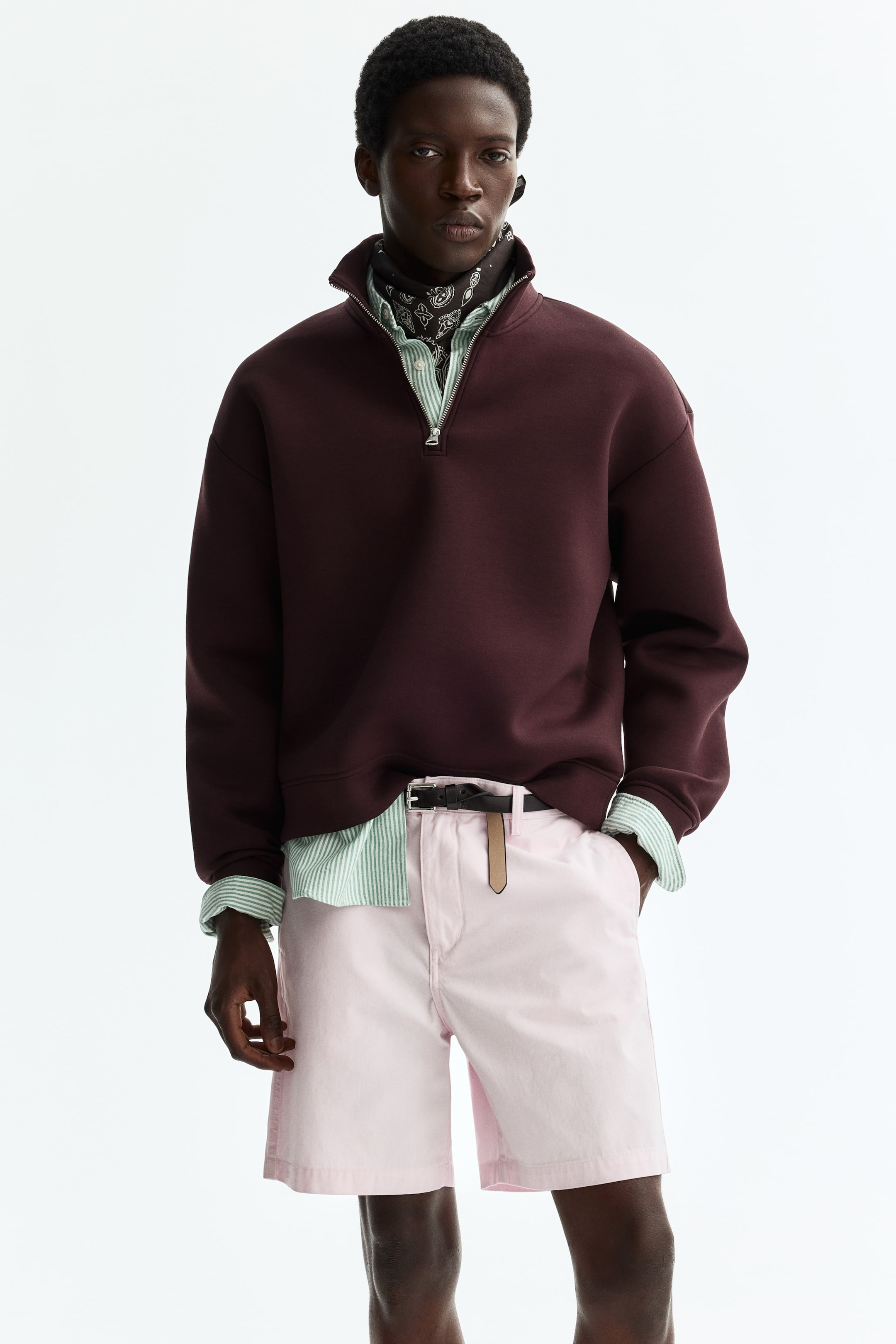 View larger image: A maroon quarter-zip sweatshirt features a high collar with a partially open silver-toned zip. A light green and white striped shirt is layered underneath, with its collar and cuffs visible, and a black patterned bandana is also visible at the neck.
