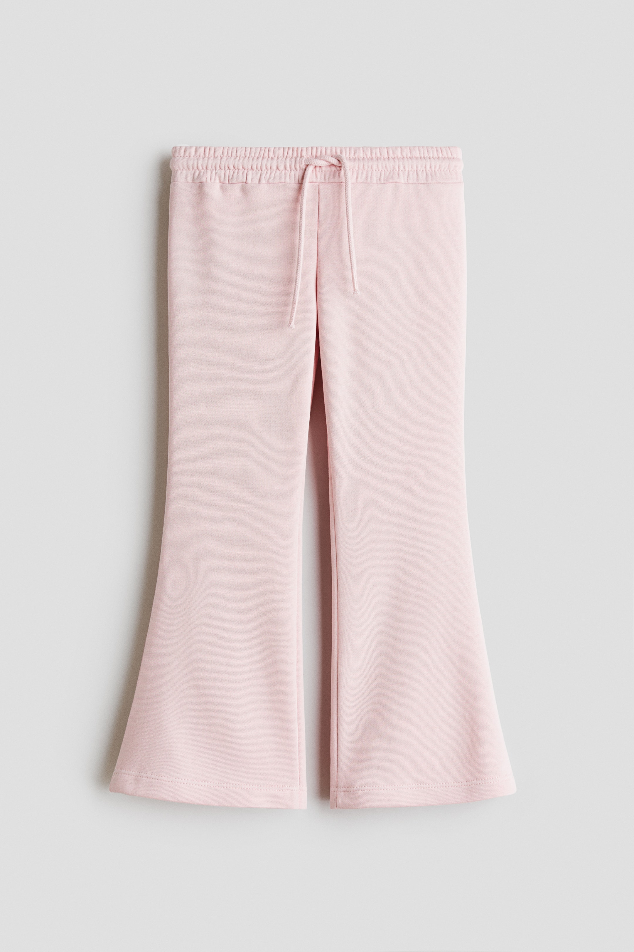 View larger image: Light pink flared pants showcase a ruched elasticated waistband, complemented by a matching drawstring tie at the center front. The legs elegantly flare from the knee to the hem.