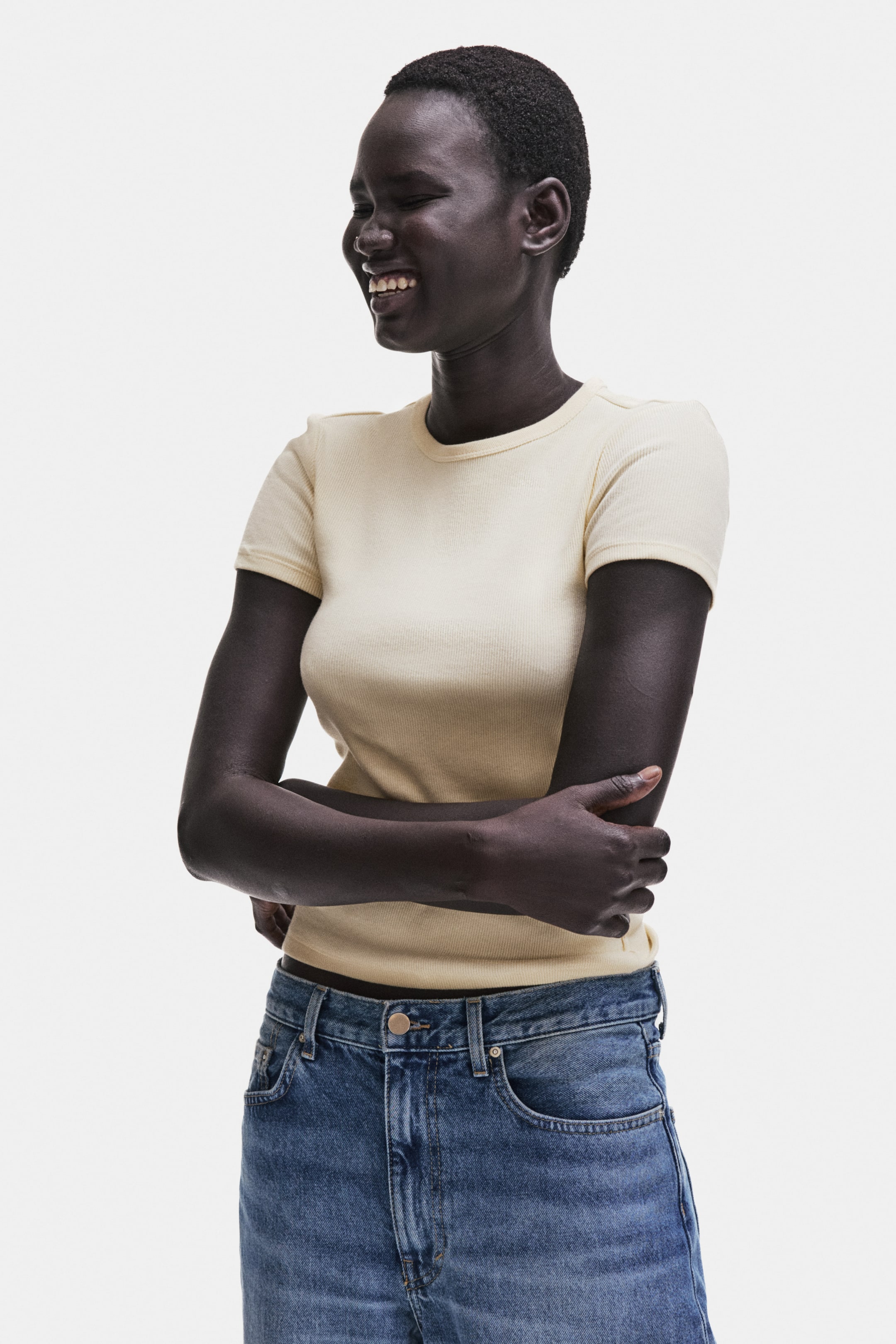 Xem ảnh lớn hơn: Một chiếc áo thun vải rib tay ngắn màu vàng nhạt đang được trưng bày, nổi bật với cổ tròn và phom ôm sát.