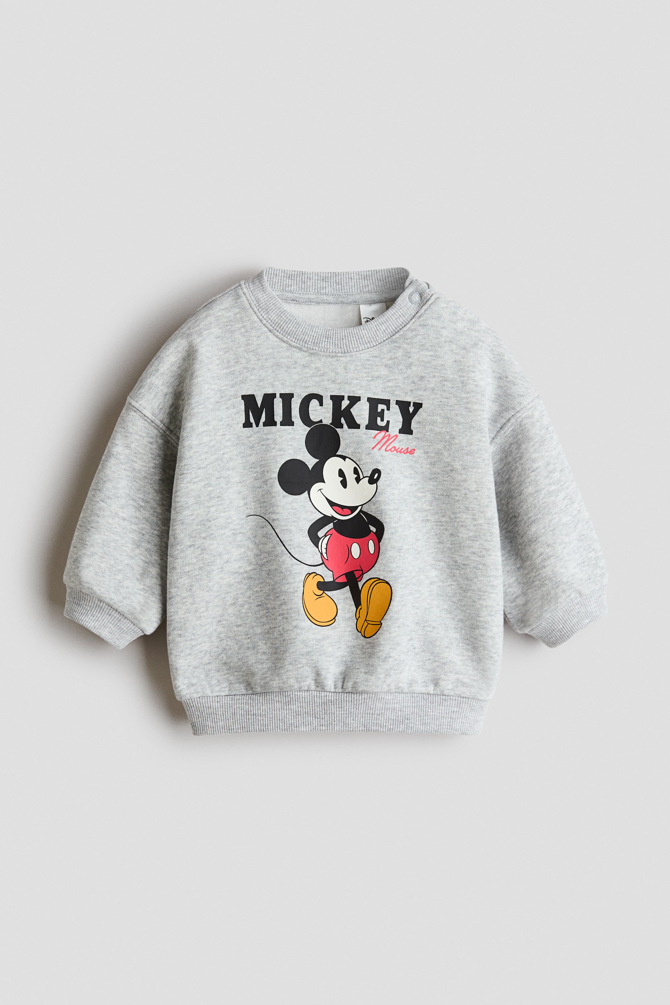 Se større billede: Printet sweatshirt. Denne lysegrå melerede sweatshirt har et grafisk print af Mickey Mouse med teksten "MICKEY Mouse" på forsiden. Den er designet med en rund halsudskæring, to trykknapper på venstre skulder og ribkanter ved ærmer og forneden.