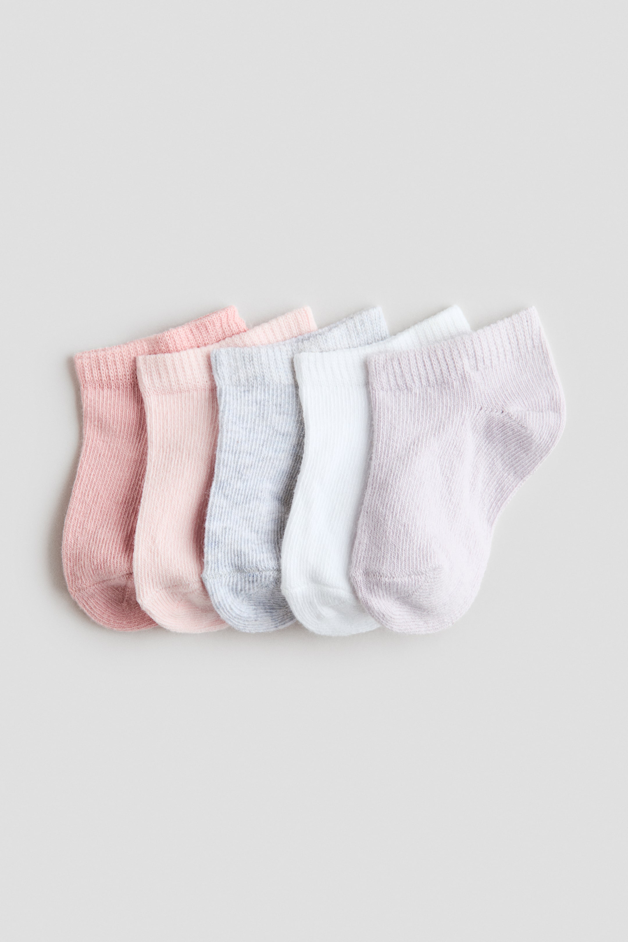 View larger image: Five trainer socks are lying in a row, displaying a fine-knit texture and ribbed cuffs. They are showcasing their side profiles in pastel shades of medium pink, light pink, light grey, white, and lilac.