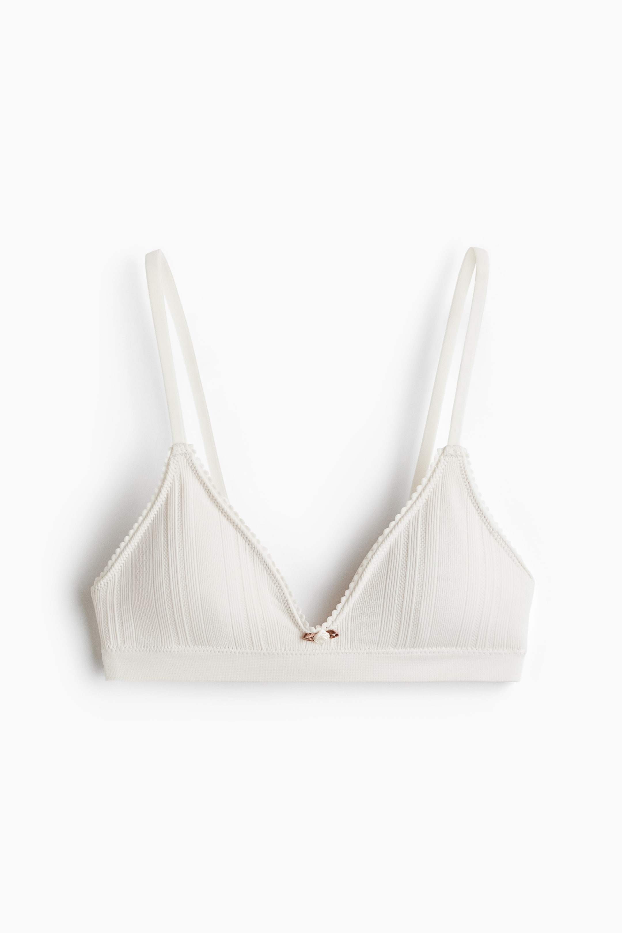 Ingrandisci l'immagine: Un reggiseno bralette color bianco sporco è mostrato dalla PARTE FRONTALE, con coppe a triangolo caratterizzate da una texture a coste verticali. Sottili spalline si estendono verso l'alto, e un bordo smerlato delinea i bordi delle coppe, con un piccolo ornamento a forma di rosa che decora la parte centrale anteriore.