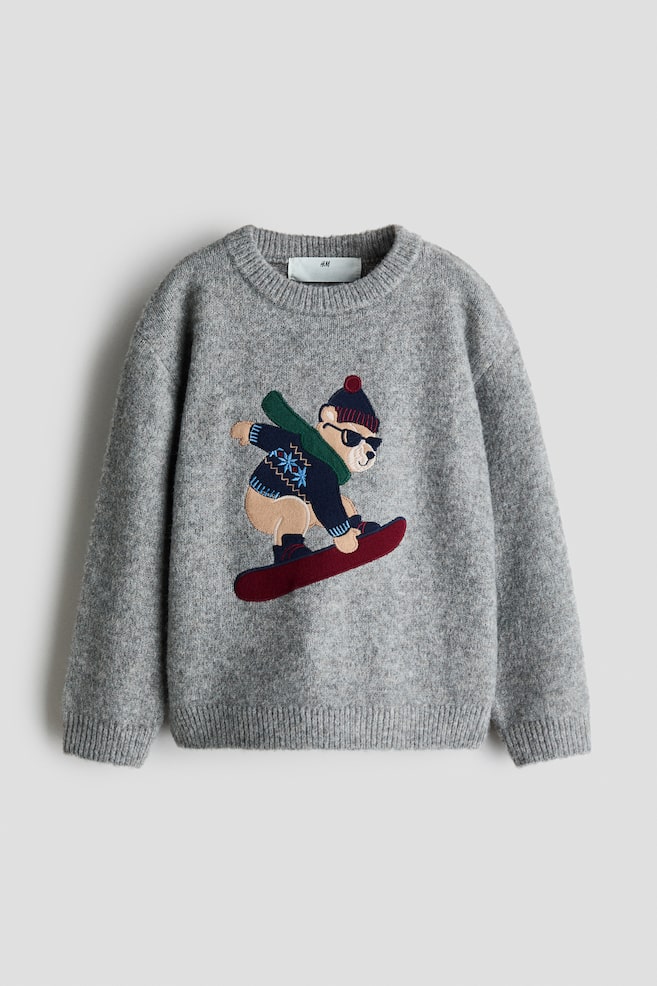 A front view of a grey heather knit jumper featuring a ribbed crew neck, cuffs, and hem. The chest displays a detailed embroidered graphic of a cartoon bear wearing a beanie, scarf, and sunglasses while riding a red snowboard. - 1