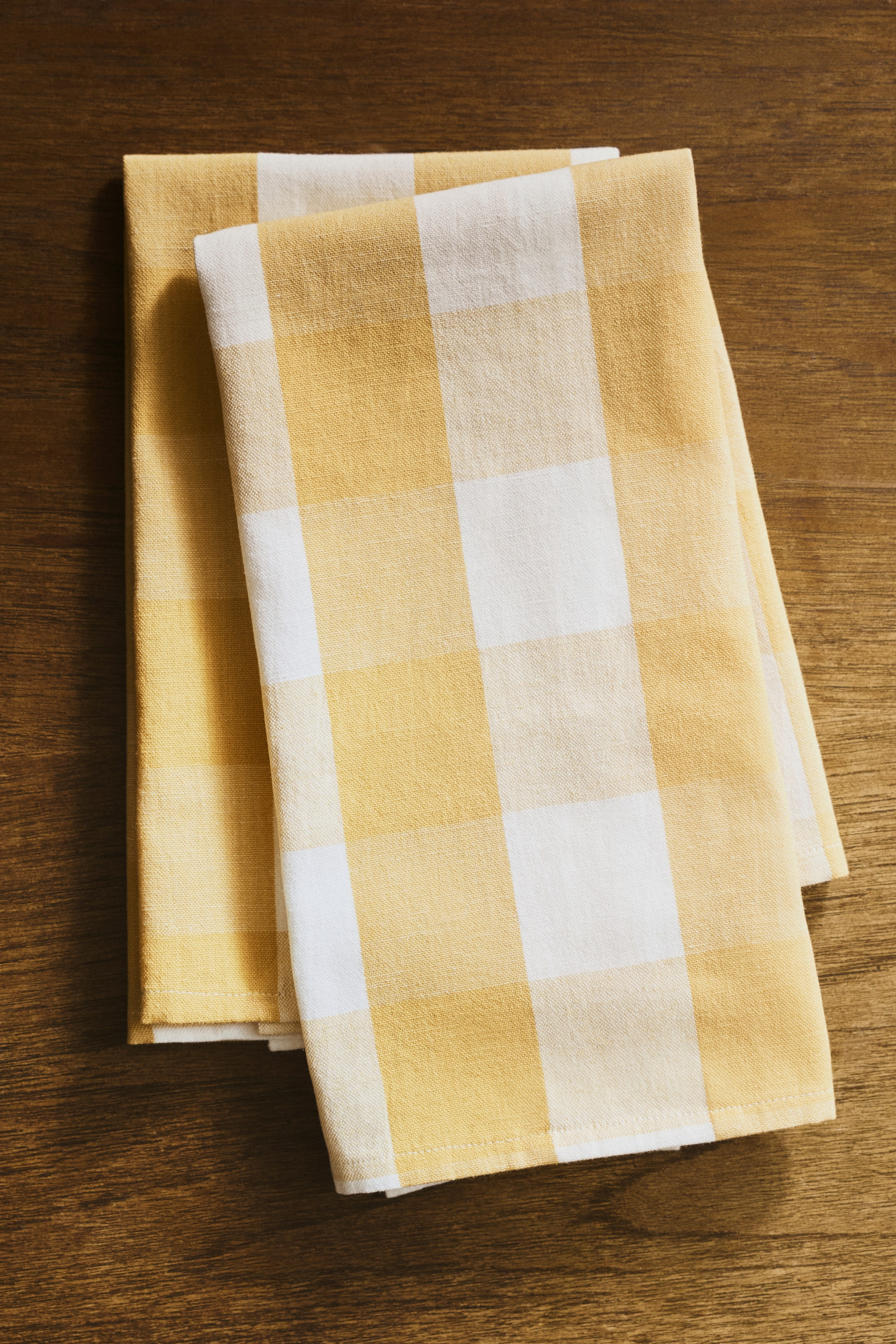 View larger image: Two tea towels are shown folded, highlighting a yellow and white gingham check pattern. The fabric features a textured weave, typical of a cotton and linen blend.