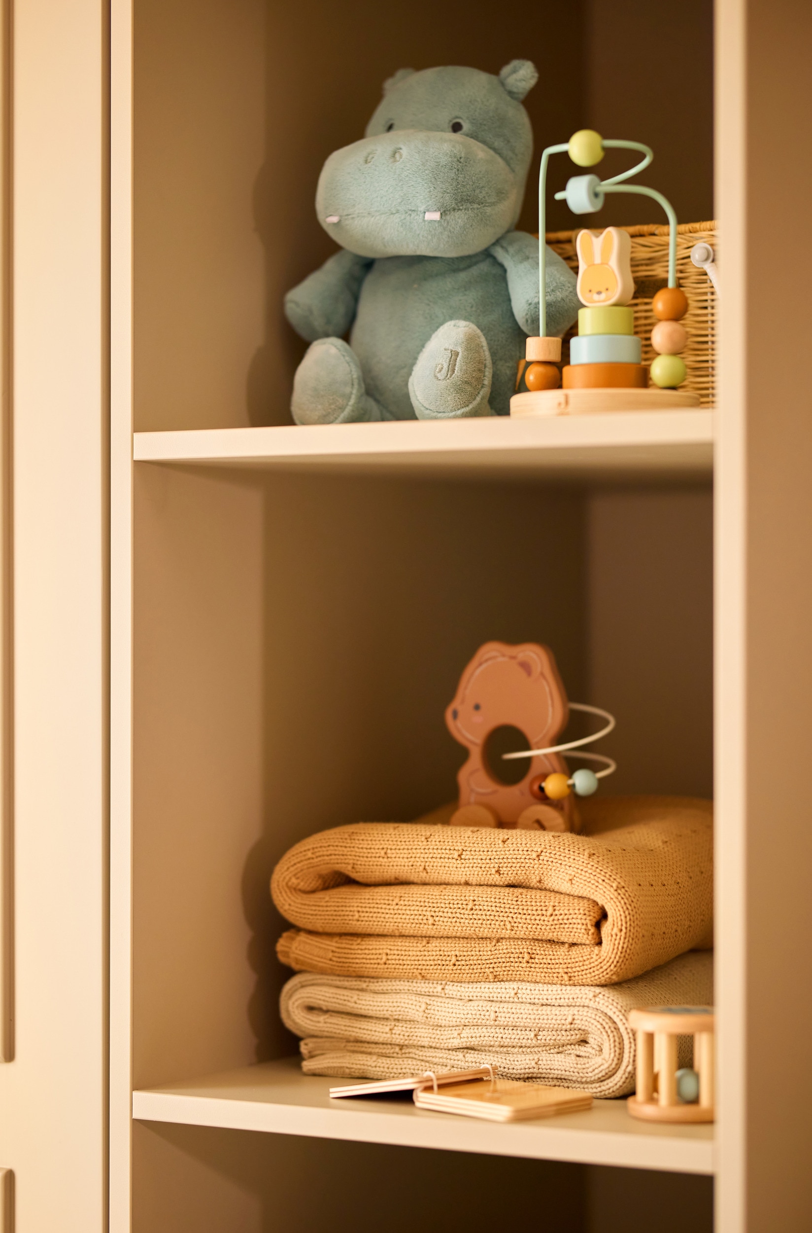 Une couverture tricotÃ©e beige est posÃ©e Ã  plat, pliÃ©e en forme rectangulaire, mettant en valeur son corps finement texturÃ© en maille et sa bordure cÃ´telÃ©e le long du bord infÃ©rieur. Une petite Ã©tiquette de marque carrÃ©e blanche, ornÃ©e dâun Â« J Â» stylisÃ©, est cousue dans le coin infÃ©rieur droit.