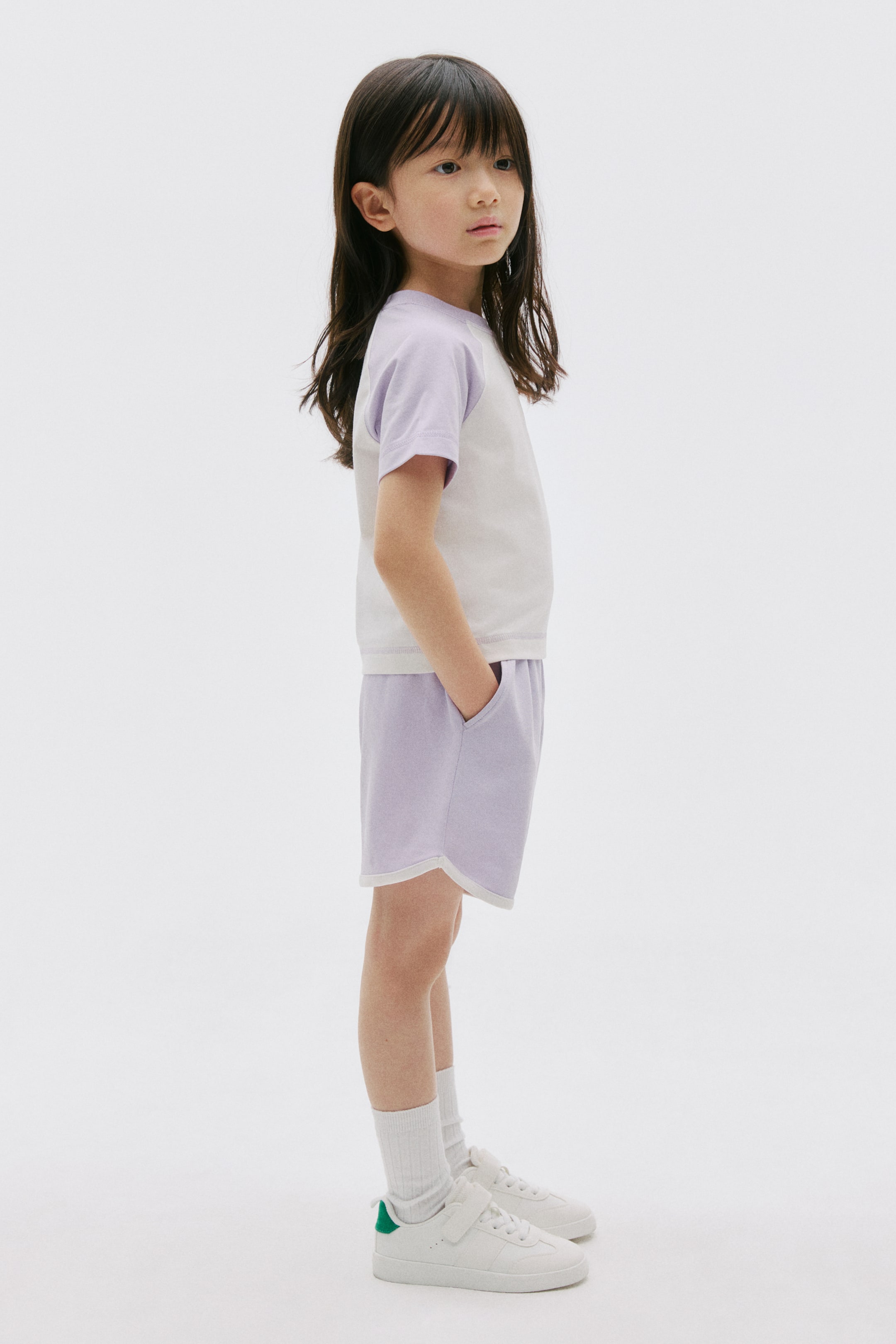 View larger image: A two-piece set is featuring a white t-shirt with light purple raglan short sleeves, paired with light purple shorts showcasing a curved white-trimmed hem and side pockets.
