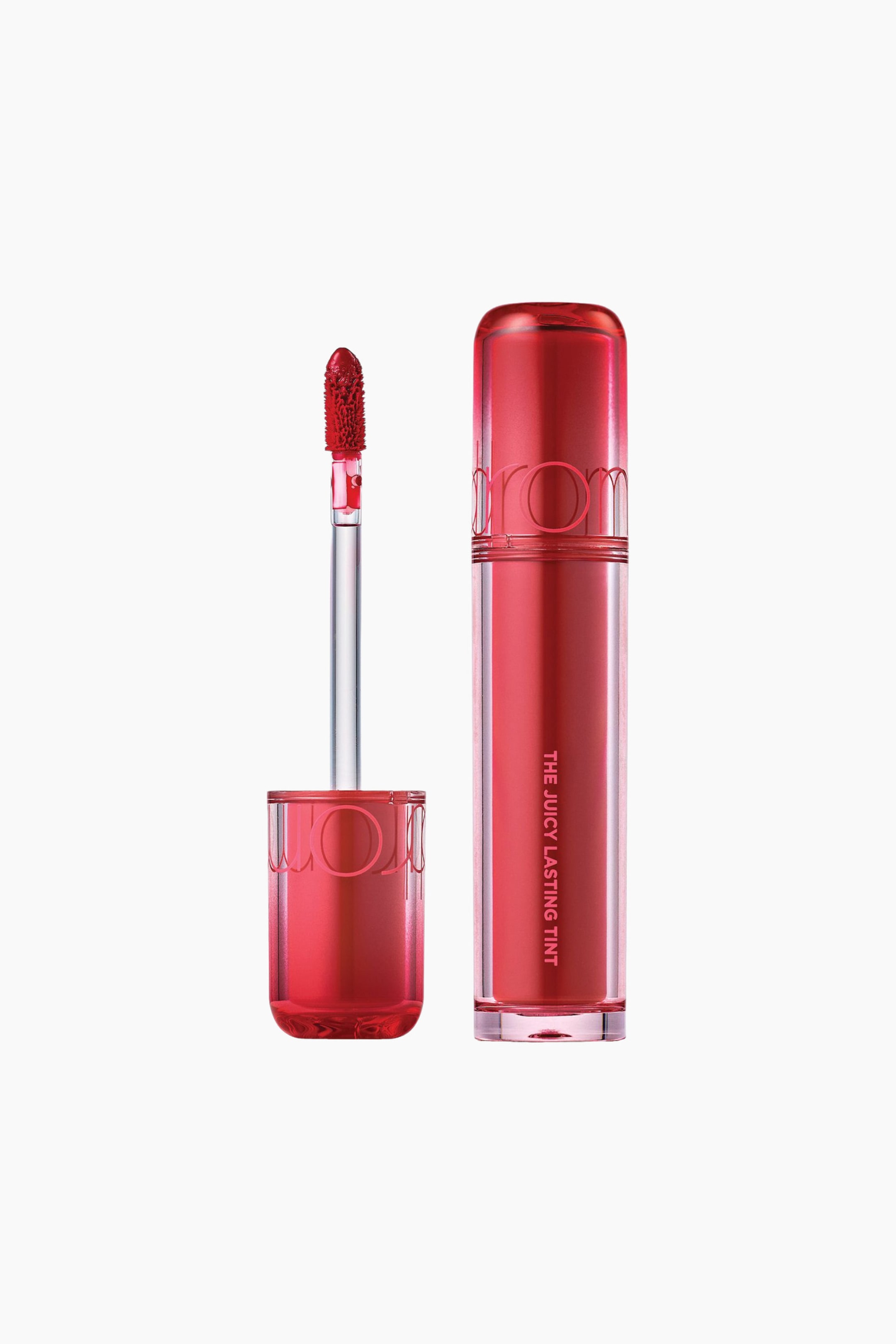Vis større bilde: Det klare, rektangulære tuben til leppefargeproduktet står oppreist, fylt med livlig rød væske, med «THE JUICY LASTING TINT» trykt vertikalt på siden og toppet med en gjennomsiktig rød kork. Den løse applikatorstaven har en rød, tintbelagt doe-foot-spiss og står oppreist i sin egen gjennomsiktige røde kork, plassert til venstre for tuben.